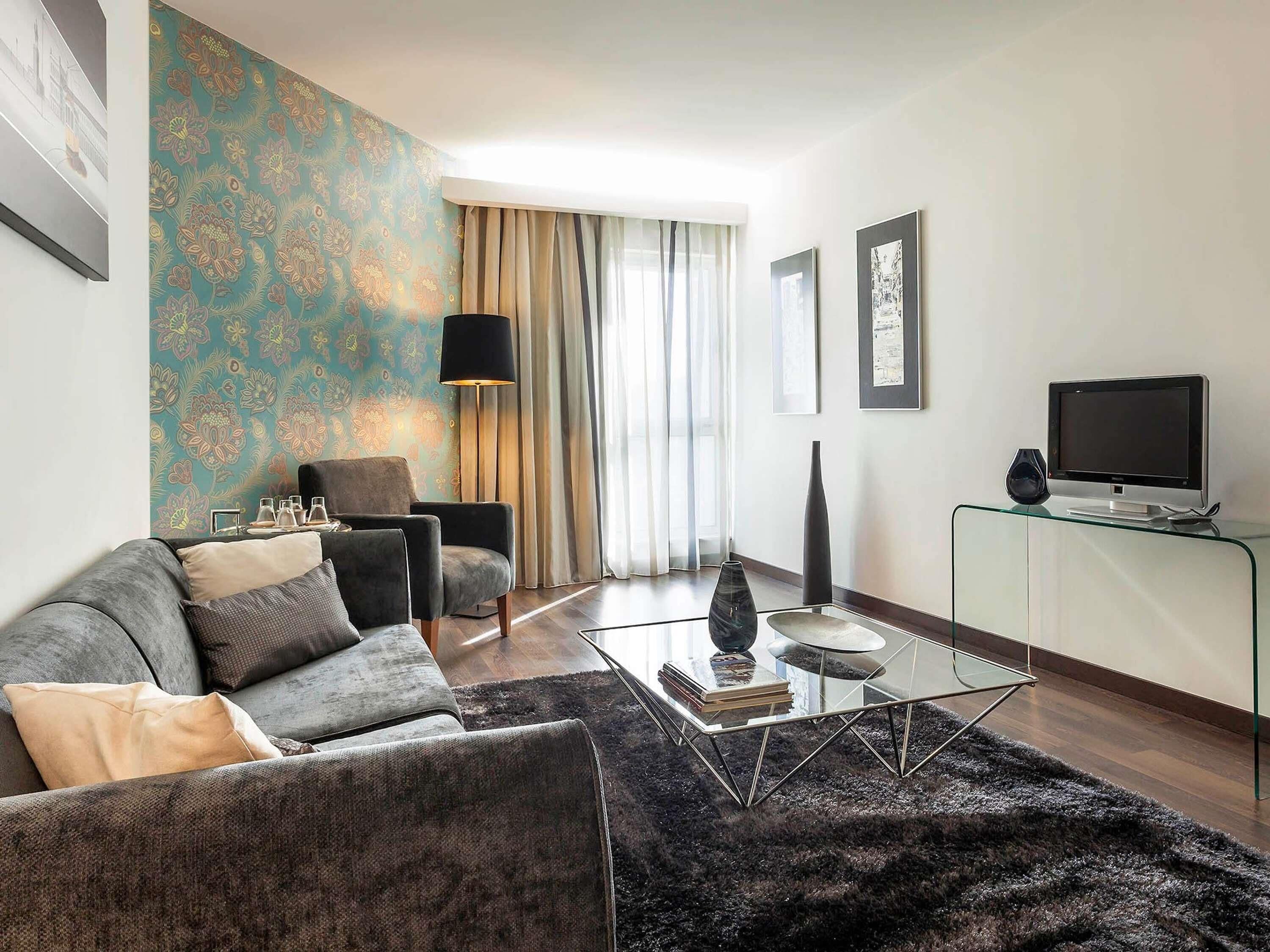 Een moderne woonkamer met een bank, fauteuil, salontafel en een televisie op een standaard.
