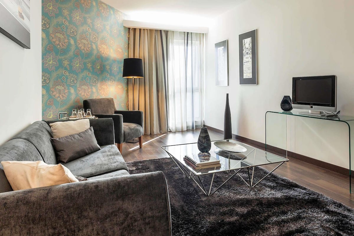 Una sala de estar moderna con sofá, sillón, mesa de centro y televisor sobre un mueble.