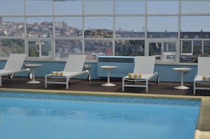 A rooftop pool area with lounge chairs and a view of the cityscape through large windows. - Mercure Lisboa Hotel (Lisbon)