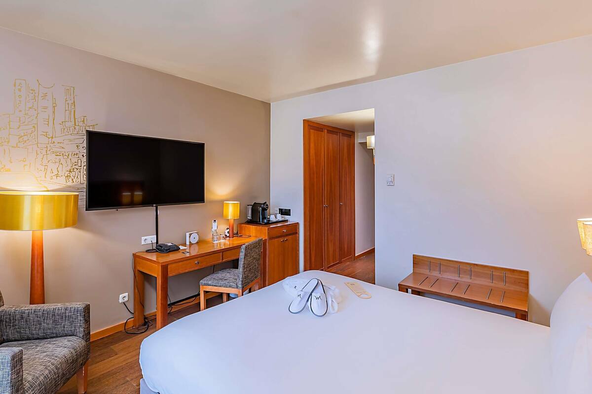Una habitación de hotel con cama, escritorio, silla, televisor y armario.
