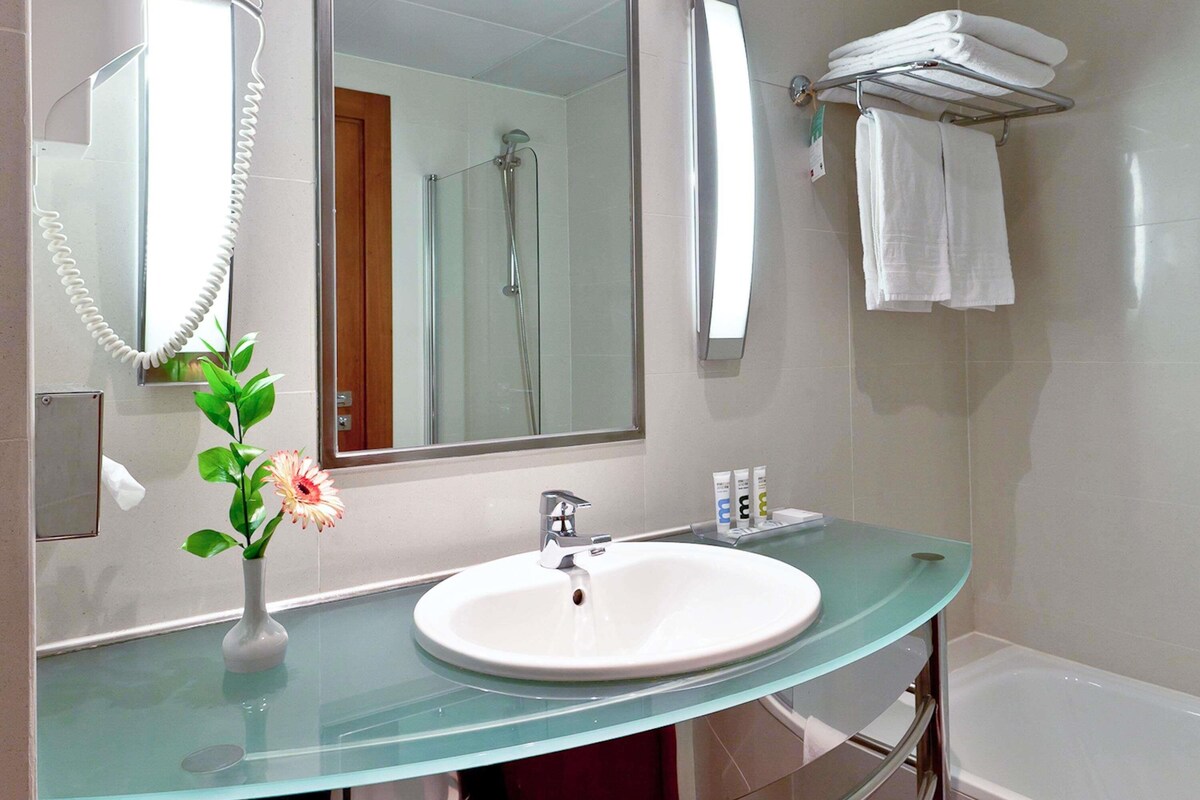 A bathroom with a glass sink, a mirror, a shower, and a towel rack.