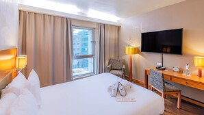 A hotel room with a bed, a desk, a chair, a TV, and a window with curtains.