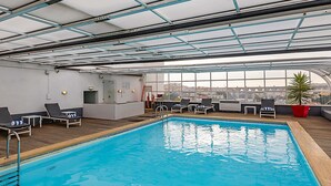 An indoor swimming pool with lounge chairs, a small bar area, and large windows offering a city view. - Mercure Lisboa Hotel (Lisbon)