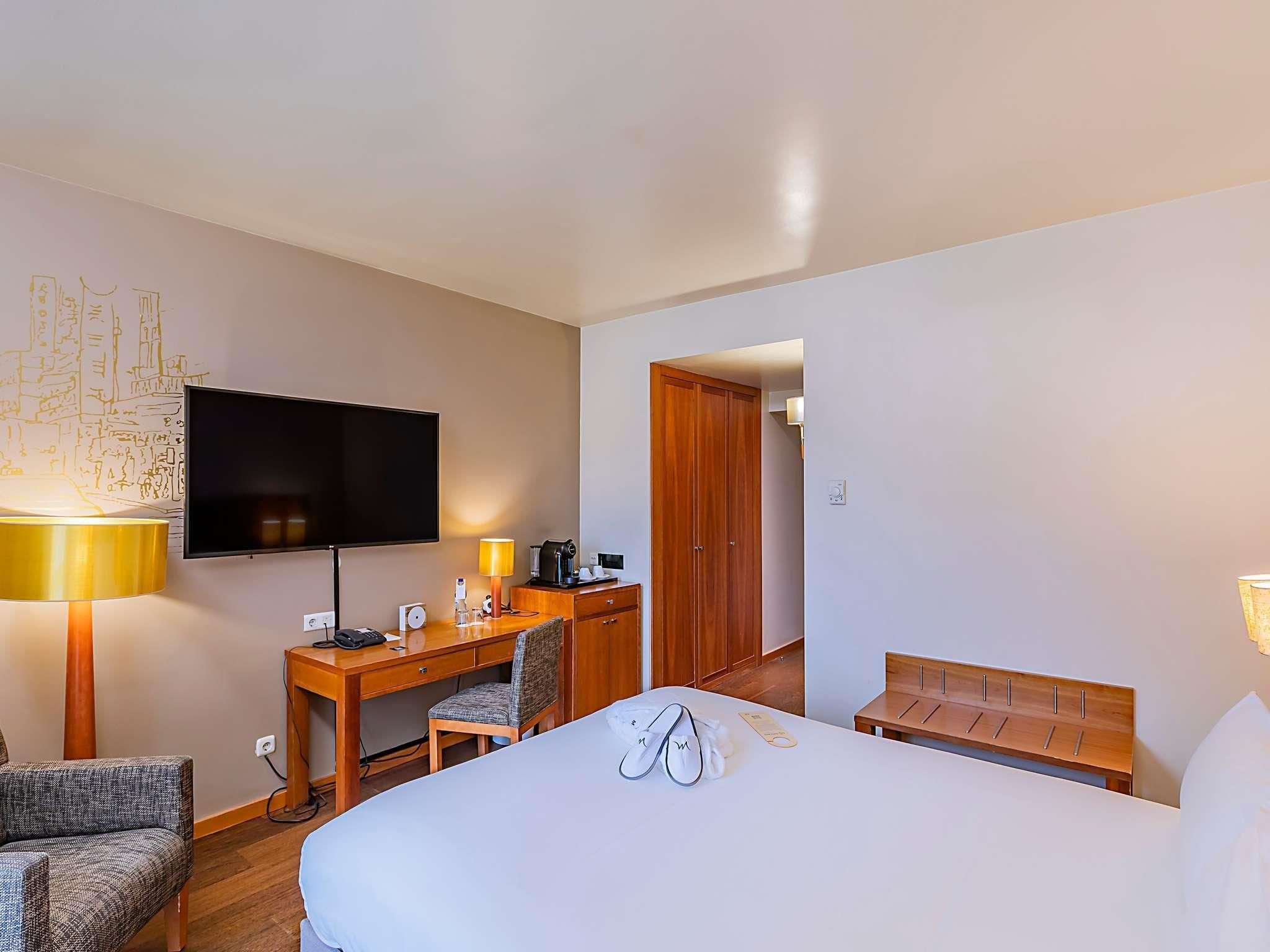 A hotel room with a bed, a desk with a chair, a television, and a wardrobe.