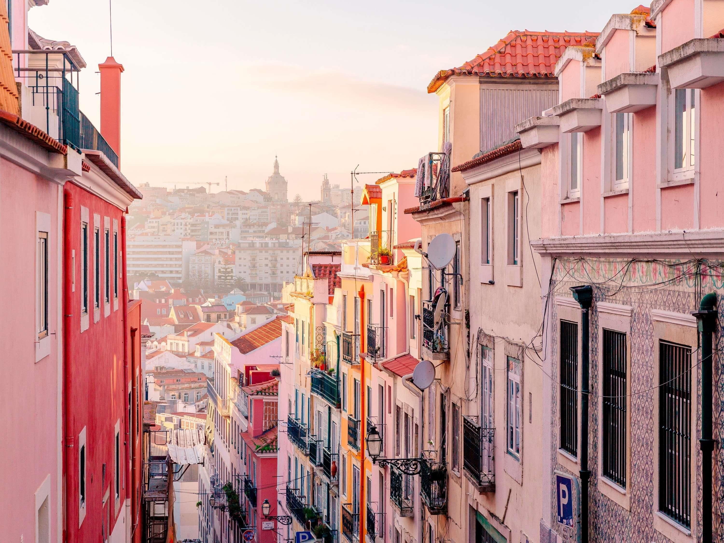 A narrow street lined with colorful buildings, a clear sky, and a distant view of a tower.