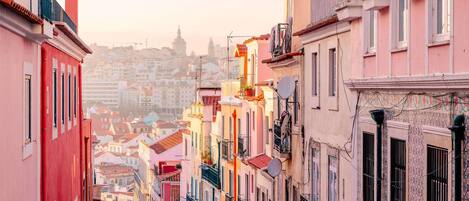 A narrow street lined with colorful buildings, a clear sky, and a distant view of a tower.