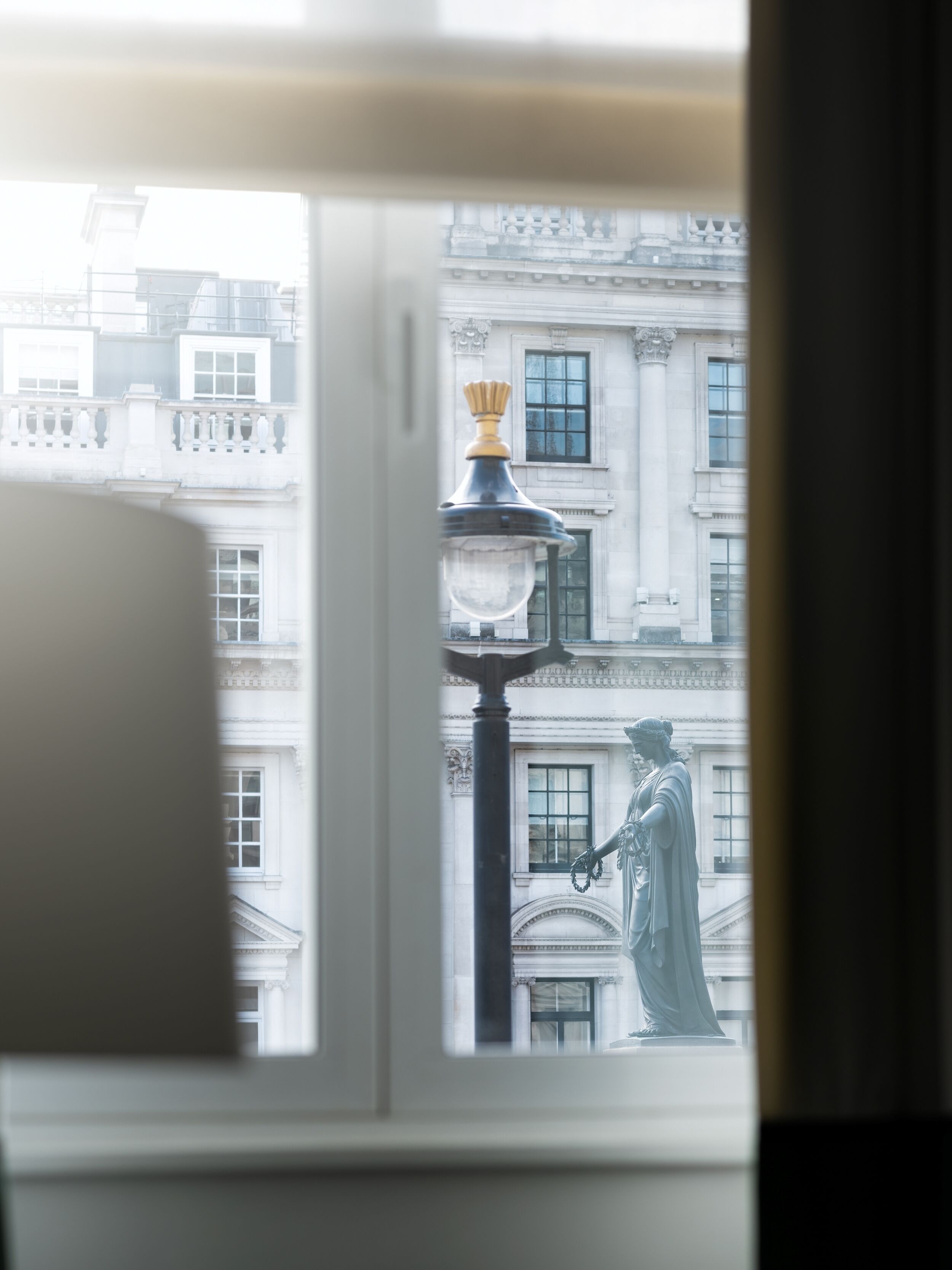 A view through a window with a street lamp and a statue outside.