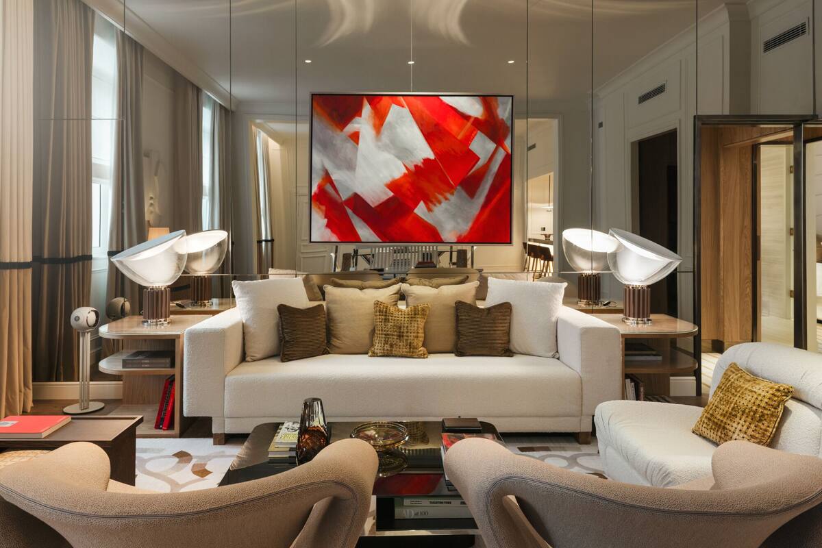 A modern living room with a white sofa, two armchairs, and a coffee table. There are two floor lamps, a flat-screen TV, and a bookshelf.