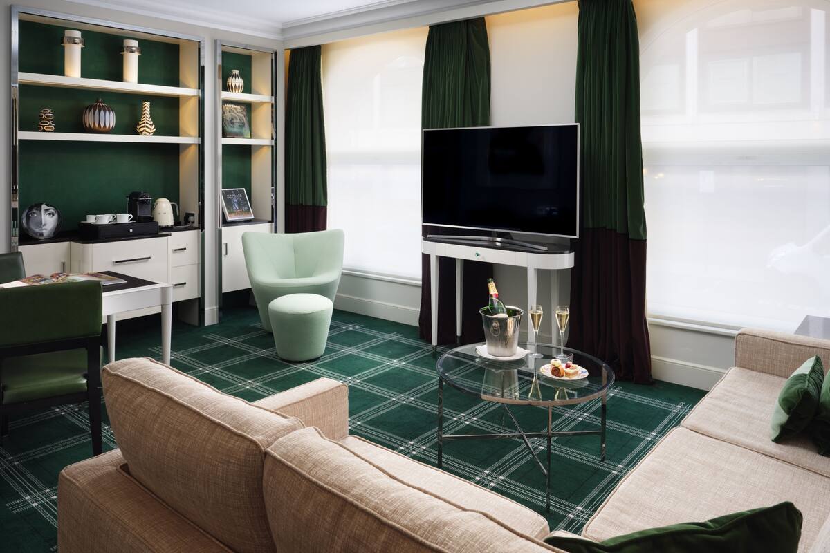A modern living room with a flat-screen TV, a green sofa, a glass coffee table, and a desk with a chair.