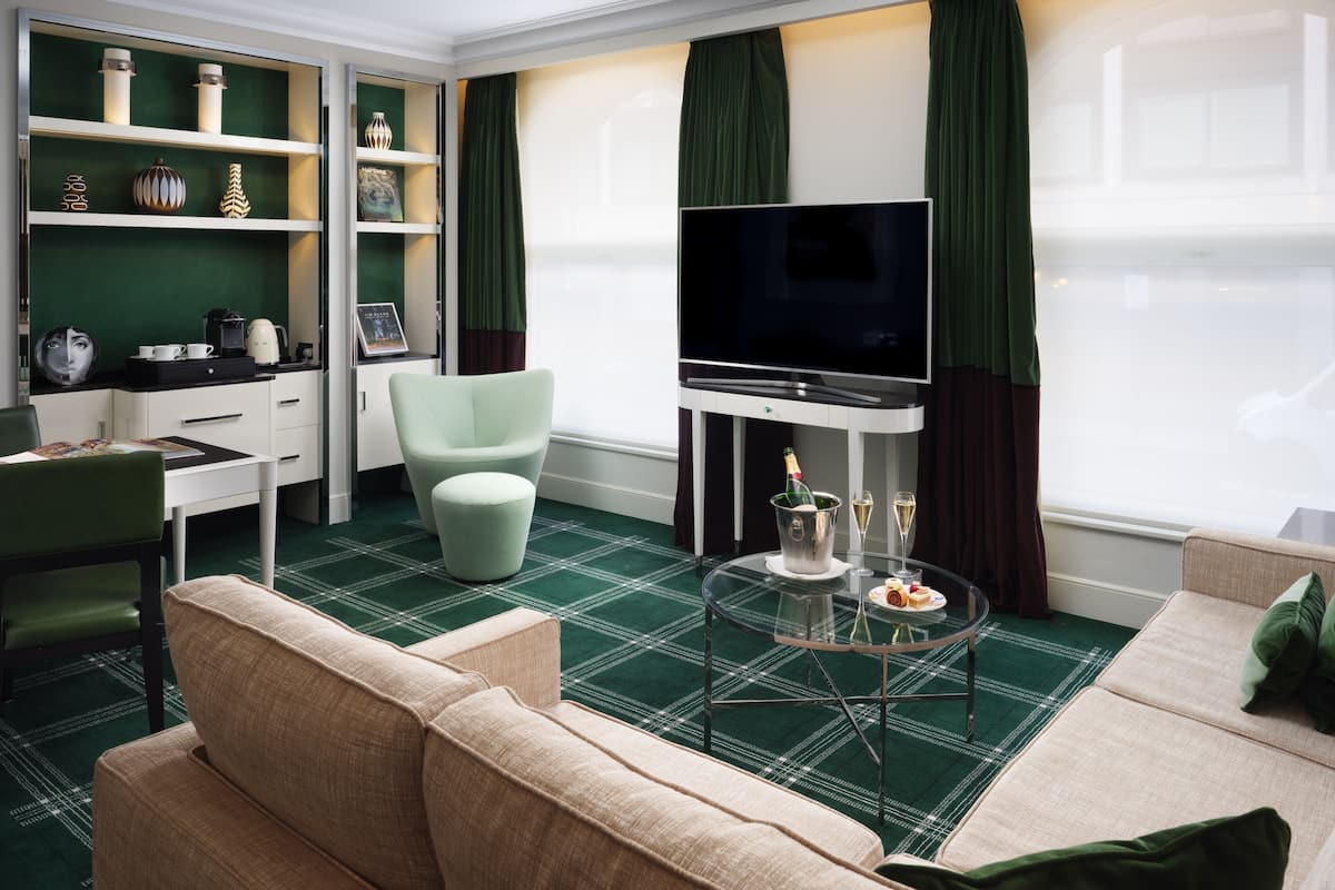 Uma sala de estar moderna com televisão de tela plana, um sofá verde, uma mesa de centro de vidro e uma escrivaninha com uma cadeira.