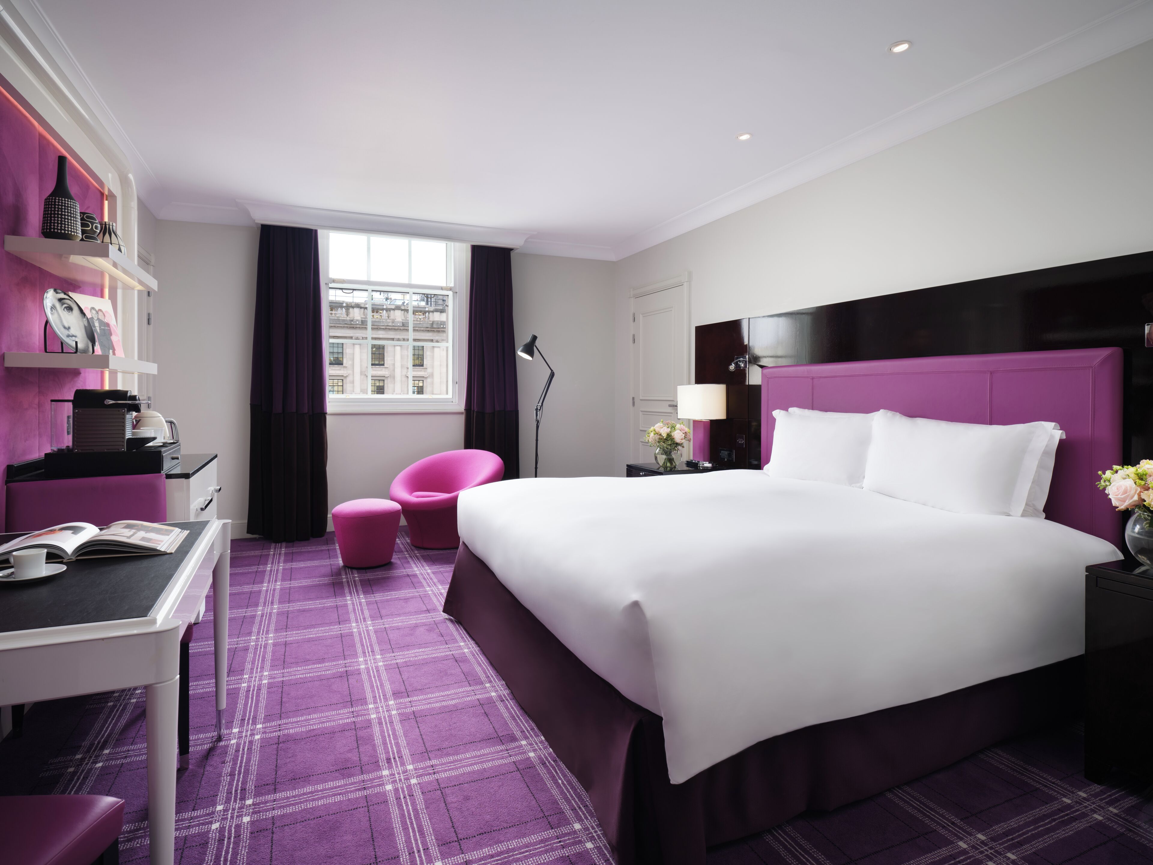 Ein modernes Hotelzimmer mit einem großen Bett, einem Schreibtisch, einem Stuhl und einem Fenster mit Blick auf die Stadt.