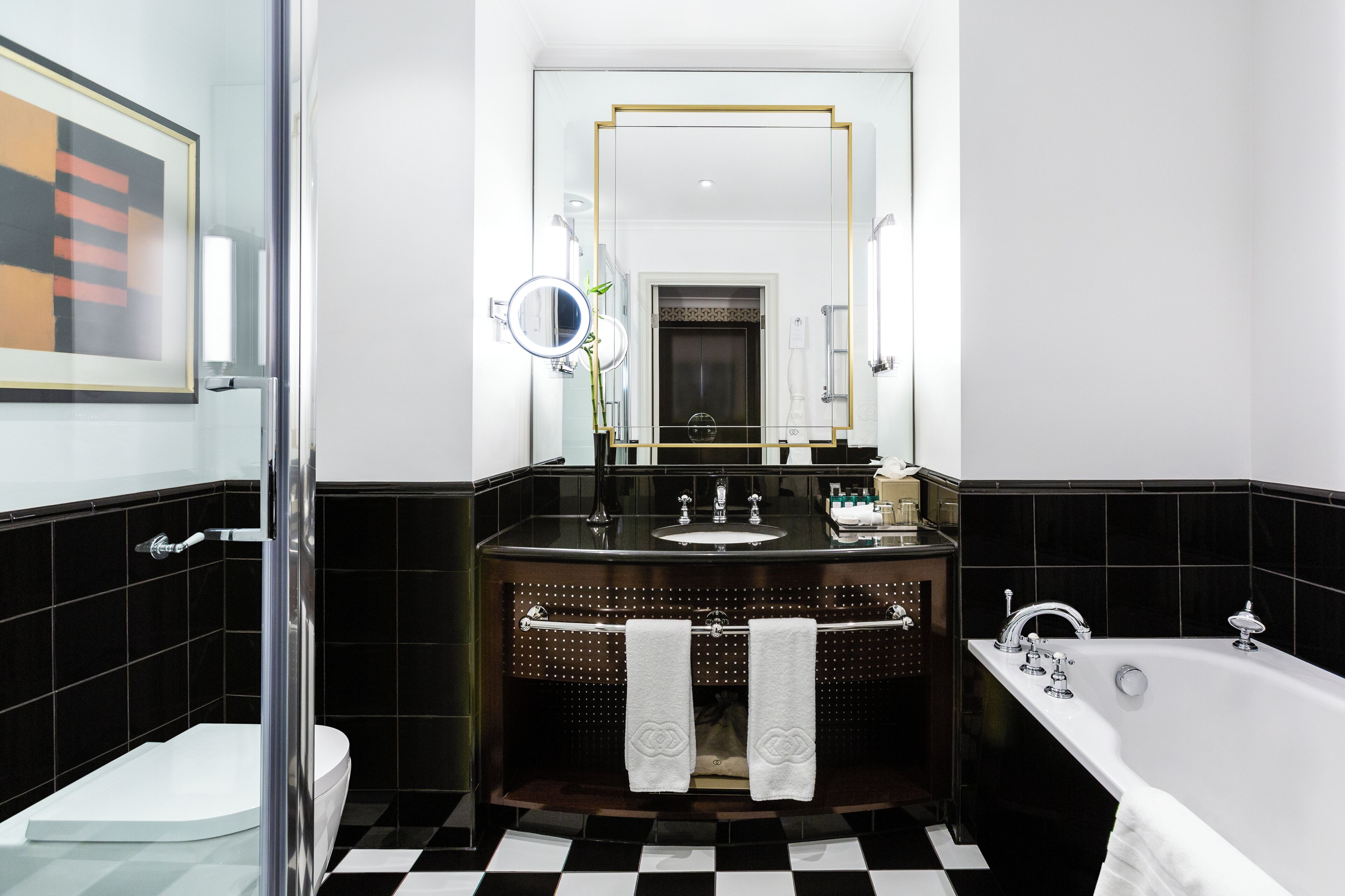 A modern bathroom with a black and white checkered floor, a glass shower enclosure, a white toilet, a black vanity with a mirror, and a white bathtub.