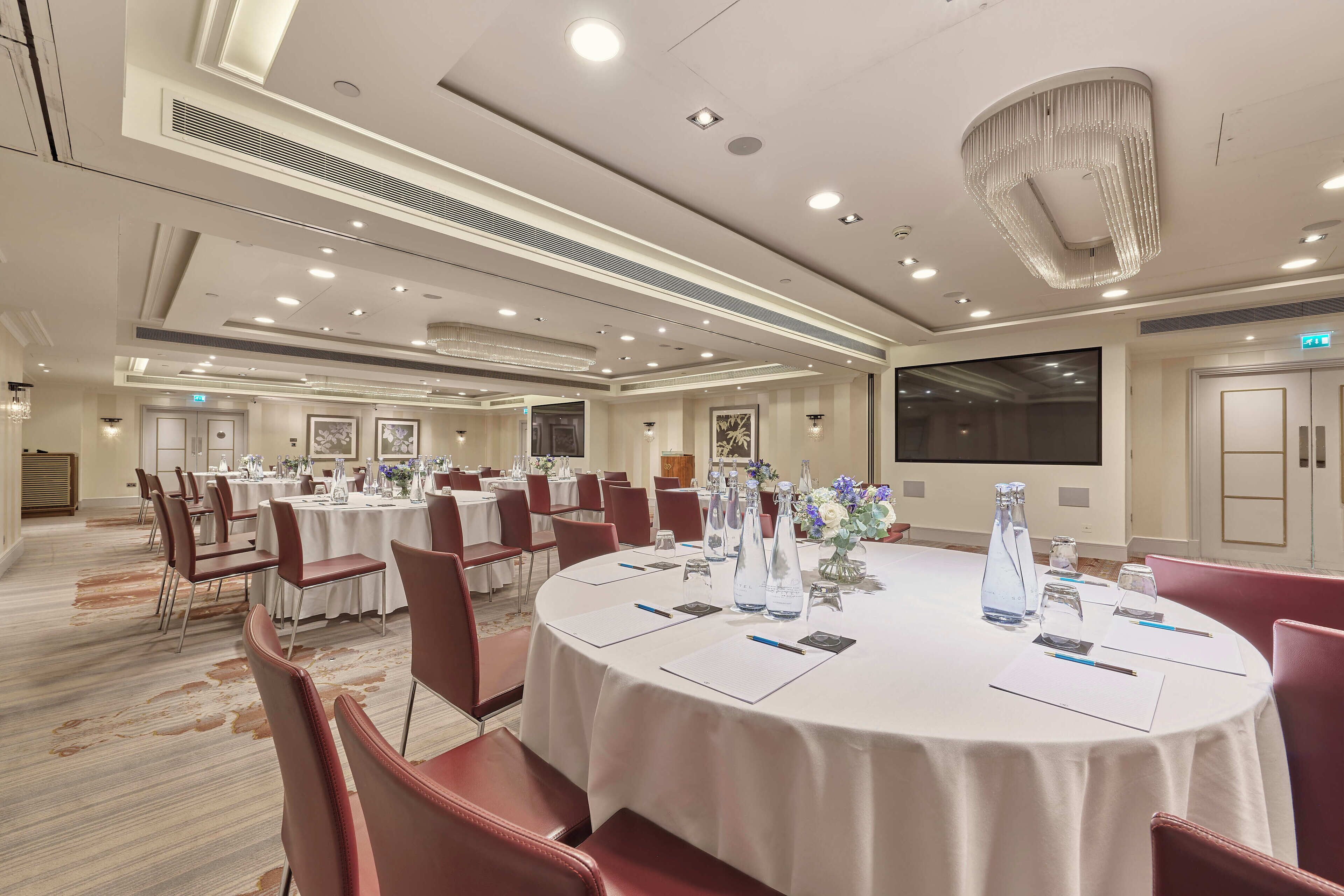 A conference room with round tables, red chairs, and white tablecloths.