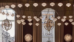 A series of hanging spherical chandeliers and a large globe chandelier in a building with arched windows and classical architecture. - Sofitel London St James (London)