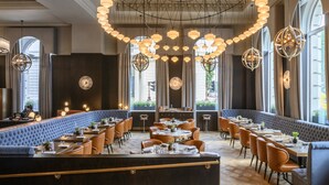 A restaurant with a long counter, multiple seating areas, and a high ceiling with decorative lighting. - Sofitel London St James (London)