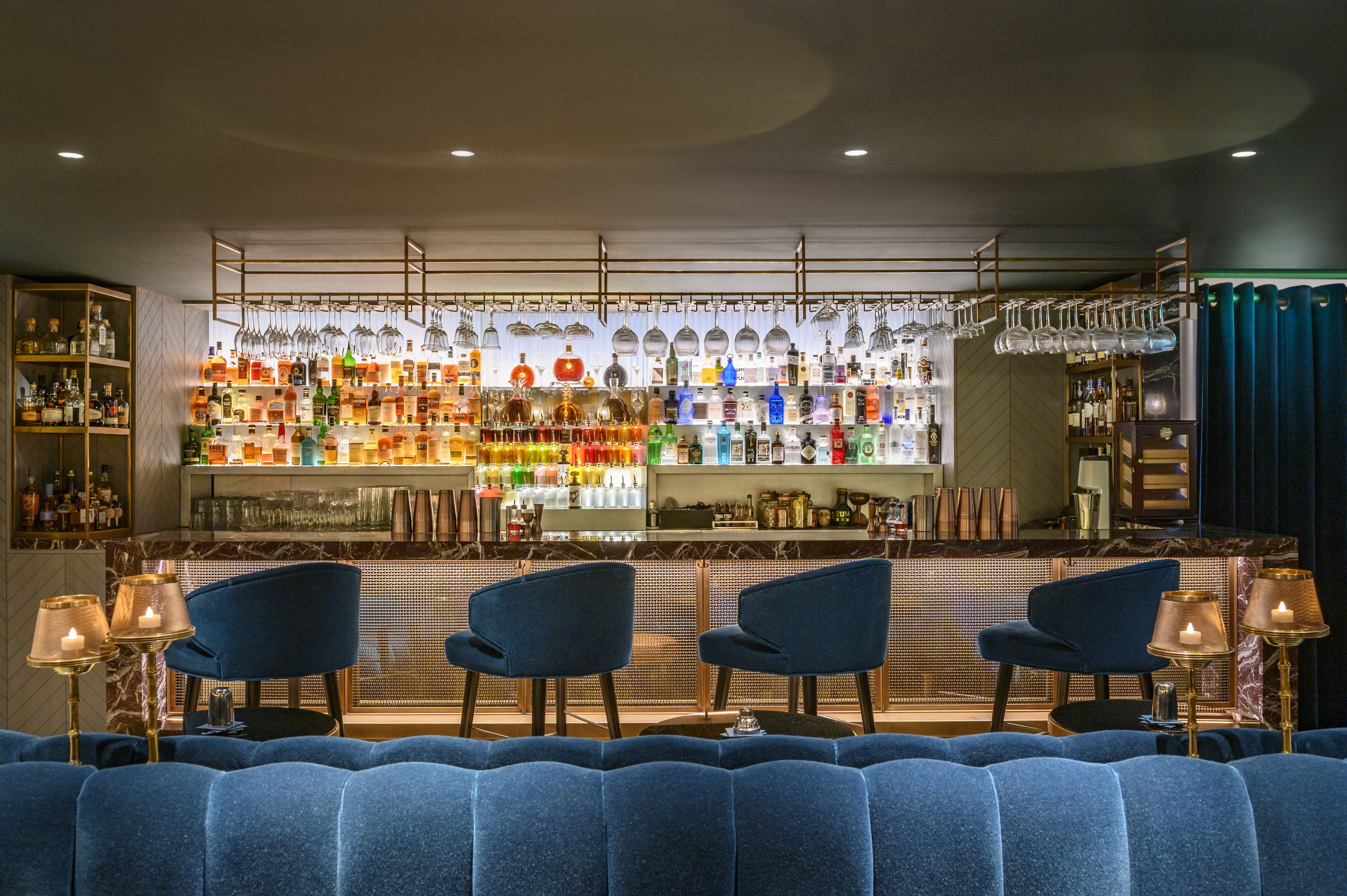 A bar area with seating and a variety of bottles and glasses on shelves.