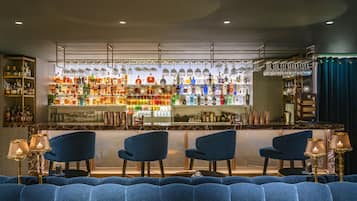 A bar area with seating and a variety of bottles and glasses on shelves.