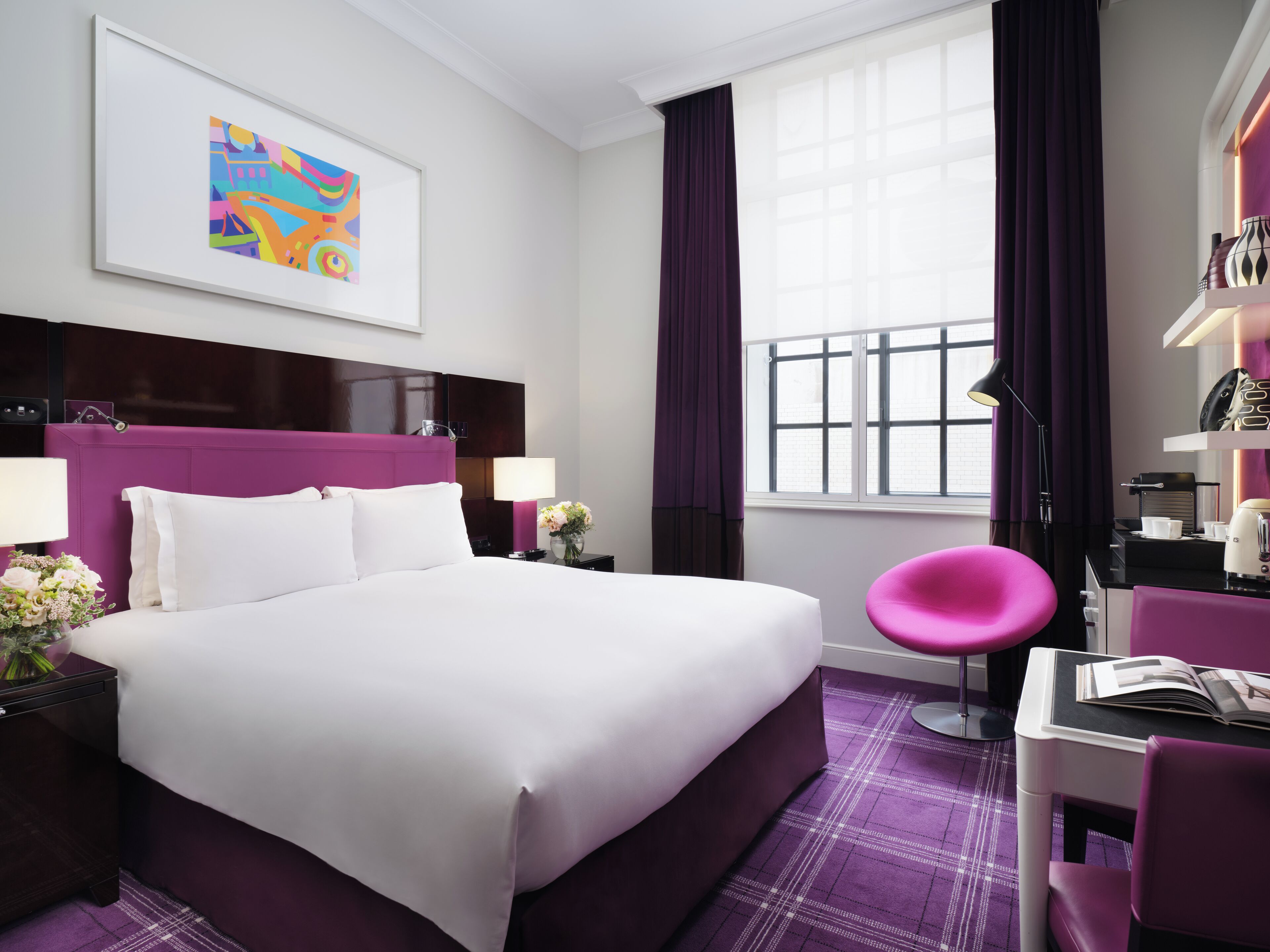 A modern hotel room with a large bed, a desk, and a chair.