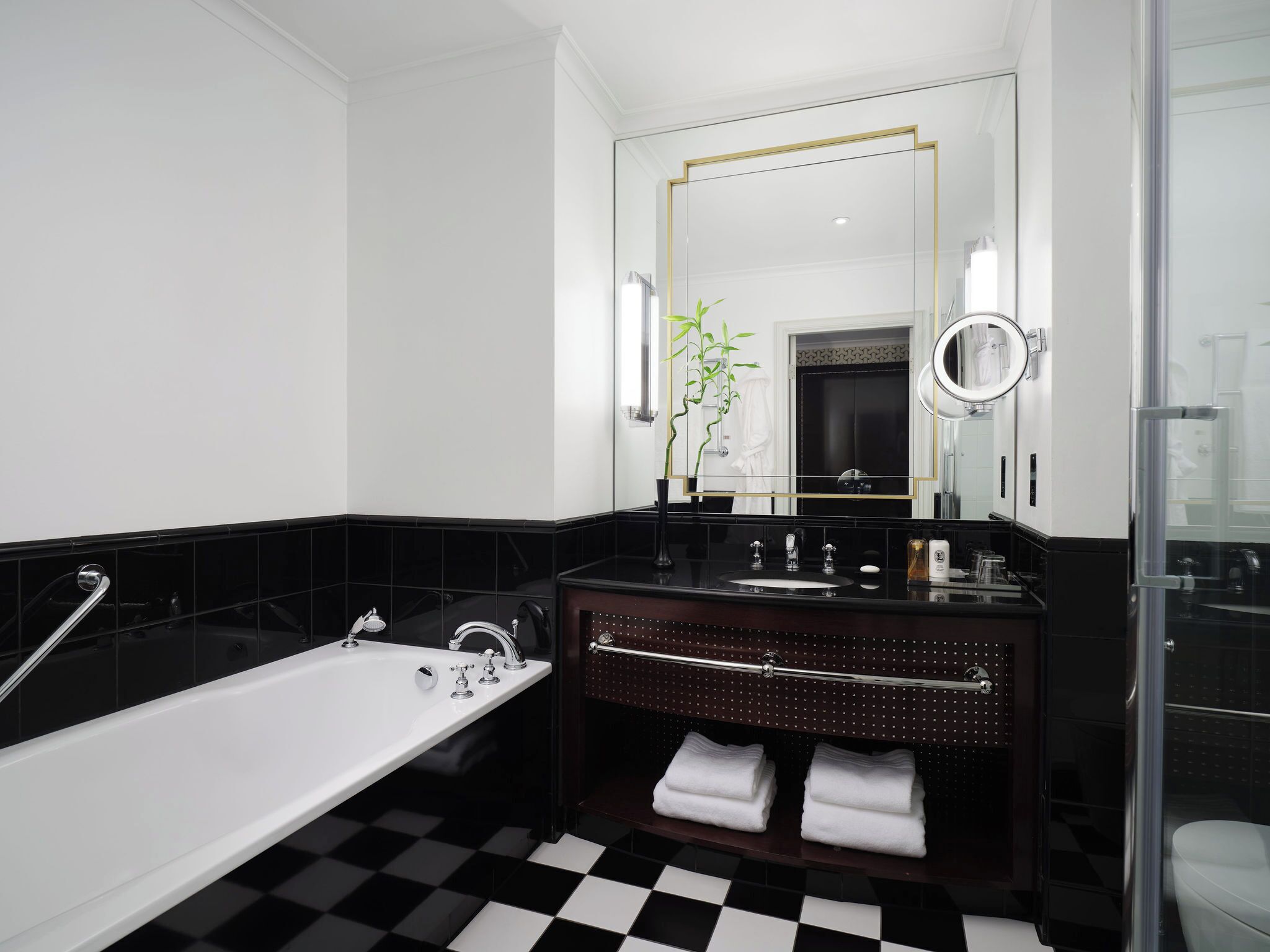 A modern bathroom with a black and white checkered floor, a white bathtub, a dark wooden vanity with a mirror, and a glass shower enclosure.