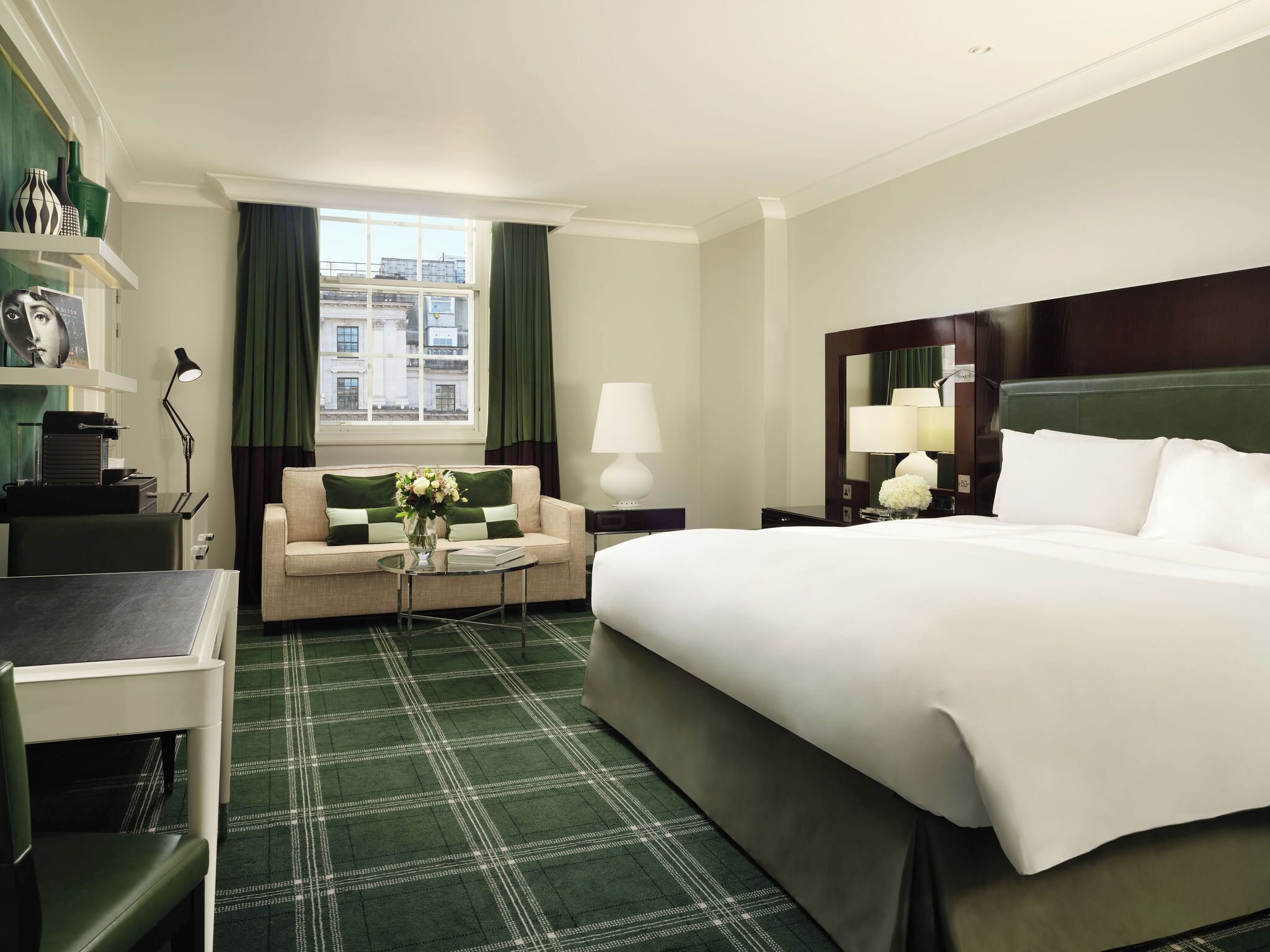 Ein Hotelzimmer mit einem großen Bett, einem Sofa, einem Schreibtisch und einem fensterbepflanzten Fenster.