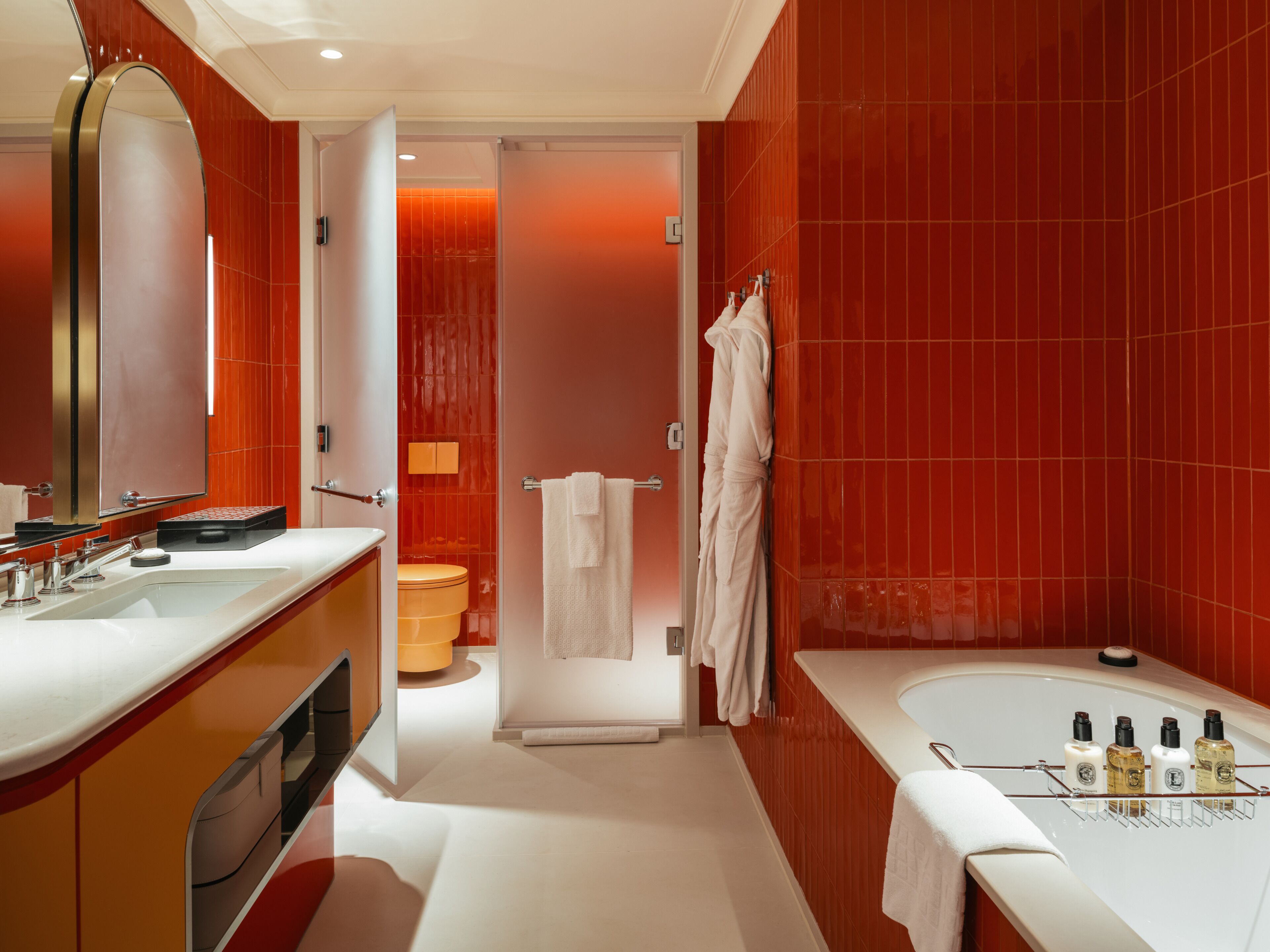 A modern bathroom with a large mirror, two sinks, a bathtub, and a toilet.