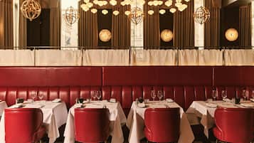 A restaurant with red upholstered booths and white tables, each set with wine glasses and cutlery.