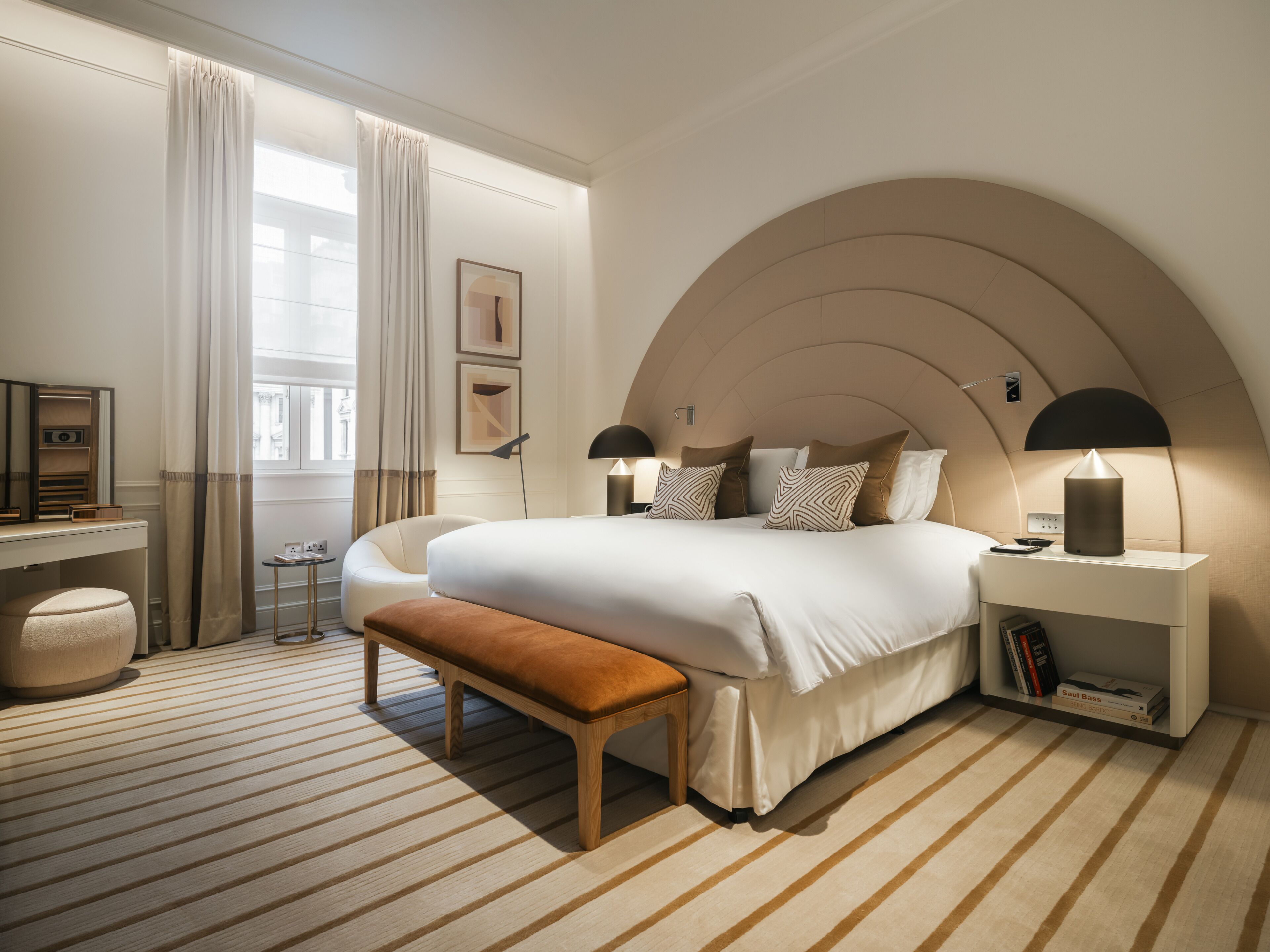 Ein modernes Schlafzimmer mit einem großen Bett, Nachttischlampen, einer Bank und einem kleinen Tisch.