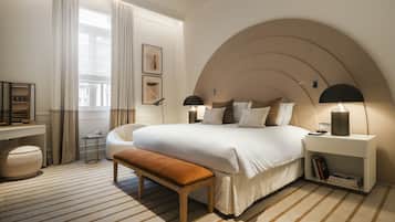Ein modernes Schlafzimmer mit einem großen Bett, Nachttischlampen, einer Bank und einem kleinen Tisch.