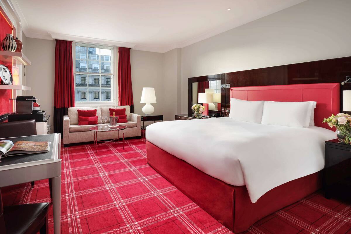 A hotel room with a large bed, a sofa, a desk, and a window with red curtains.