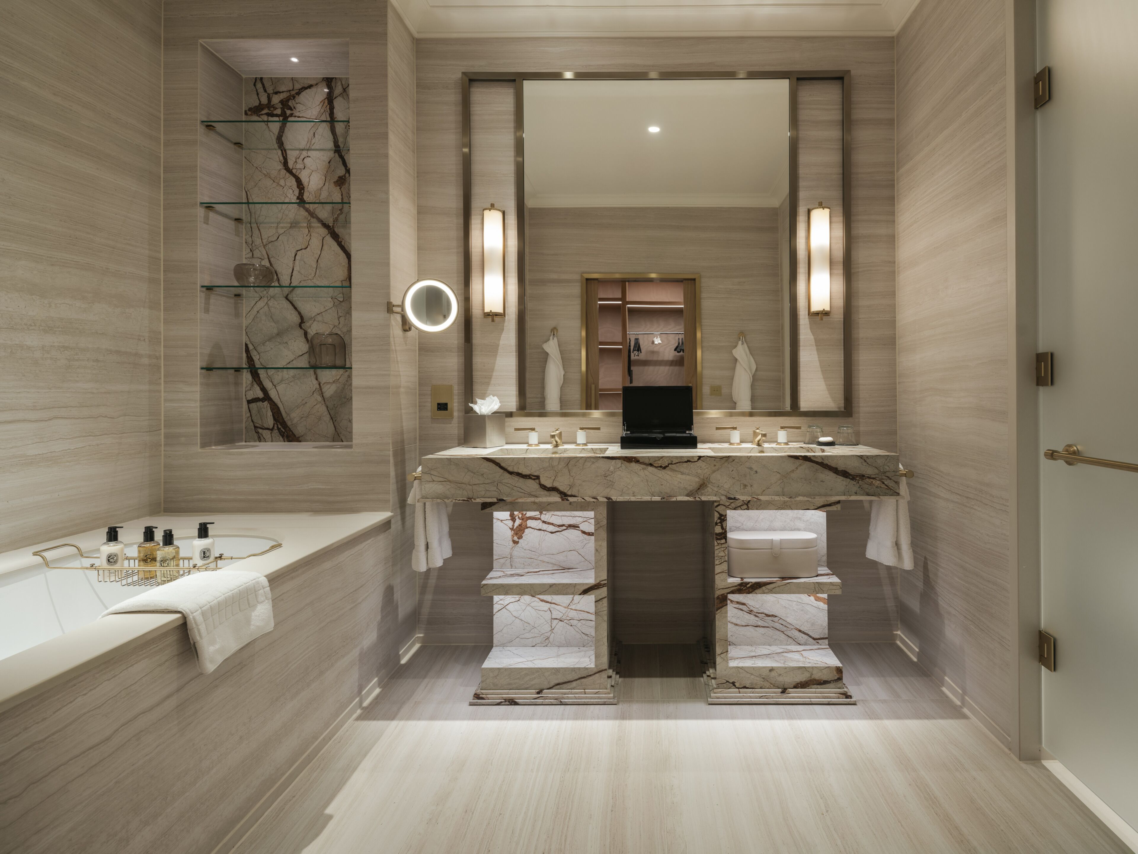 A modern bathroom with a marble vanity, a large mirror, and a built-in bathtub.