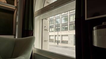 A room with a large window, a chair, and a metal container.