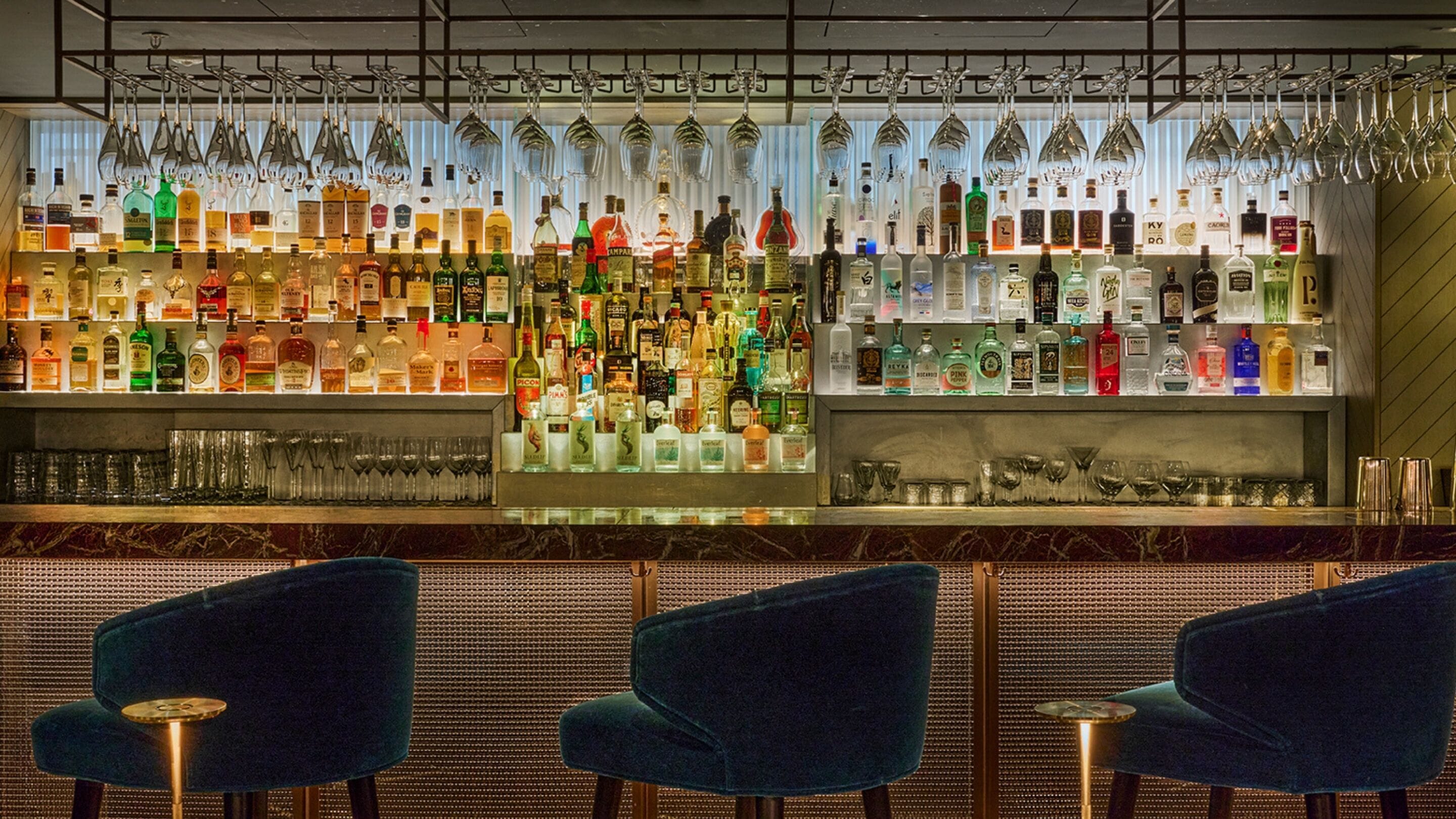 A bar area with multiple liquor bottles and glasses, and three blue chairs.