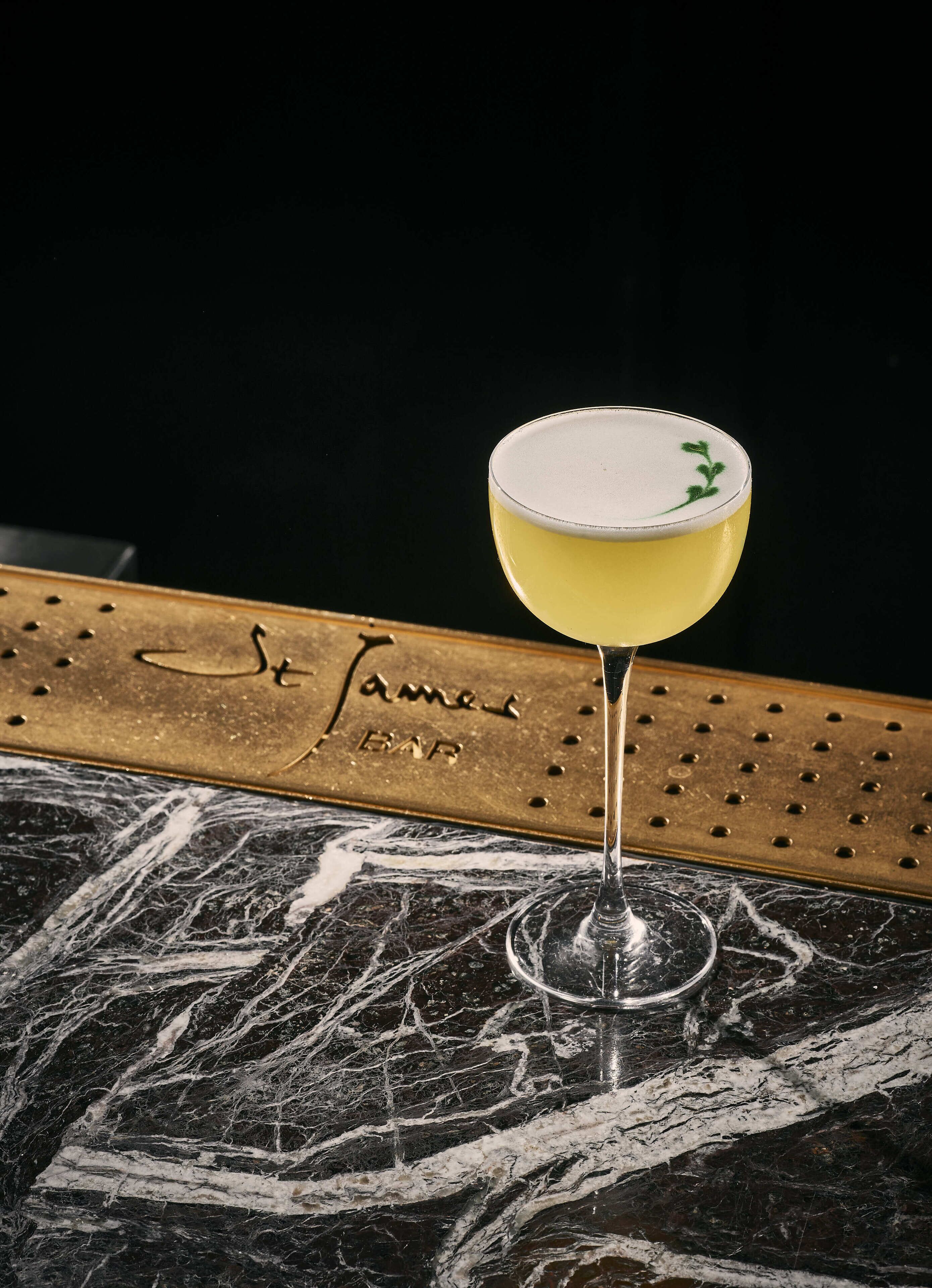 Um copo de martini com líquido amarelo sobre uma superfície de mármore.