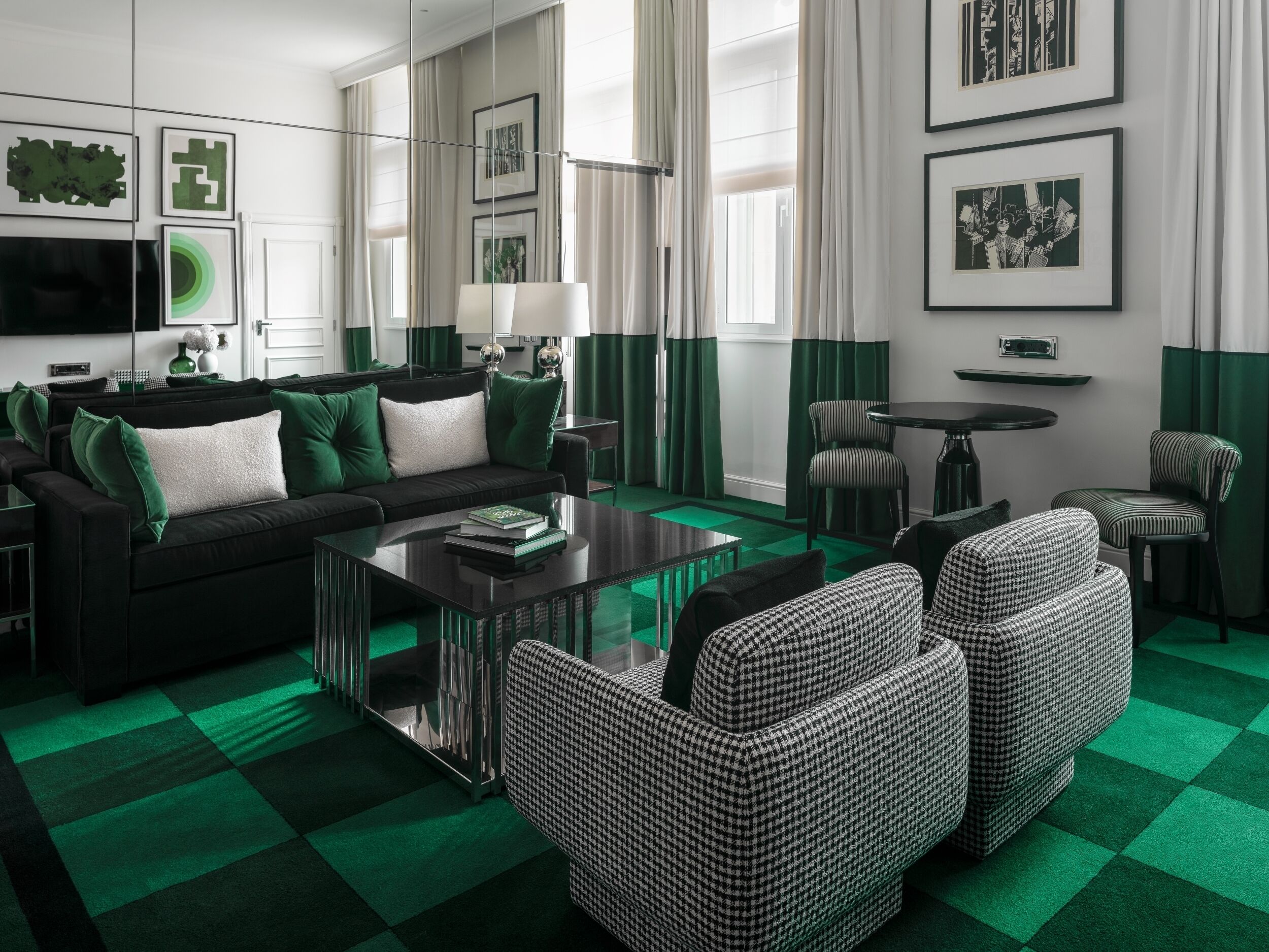 A modern living room with a black sofa, green cushions, a glass coffee table, and a checkered green carpet.