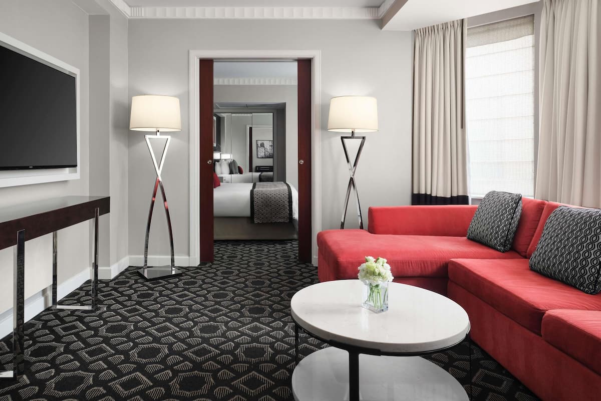 A hotel room with a red sofa, a round coffee table, a TV, and two floor lamps.