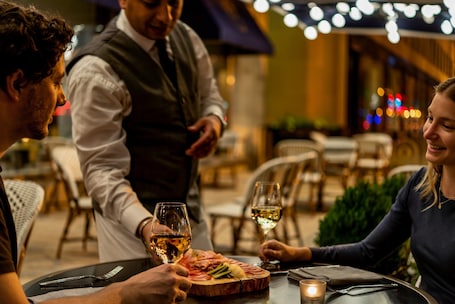 A dining table with a wooden board of food, two glasses of white wine, and a lit candle.