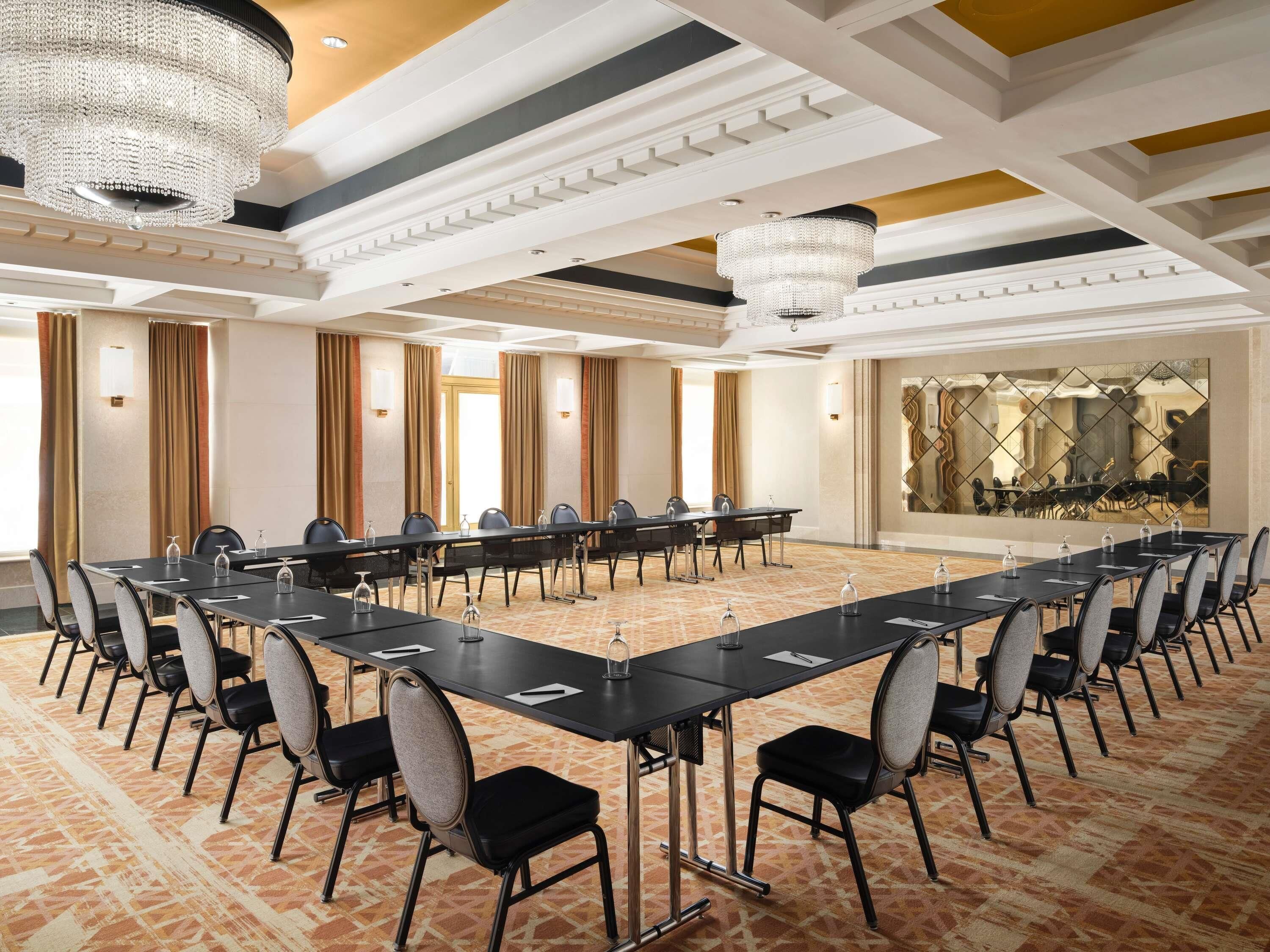 A conference room with a long table, chairs, chandeliers, and a patterned carpet.