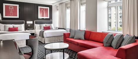 A modern hotel room with a large bed, a red sofa, two small tables, and a patterned rug.