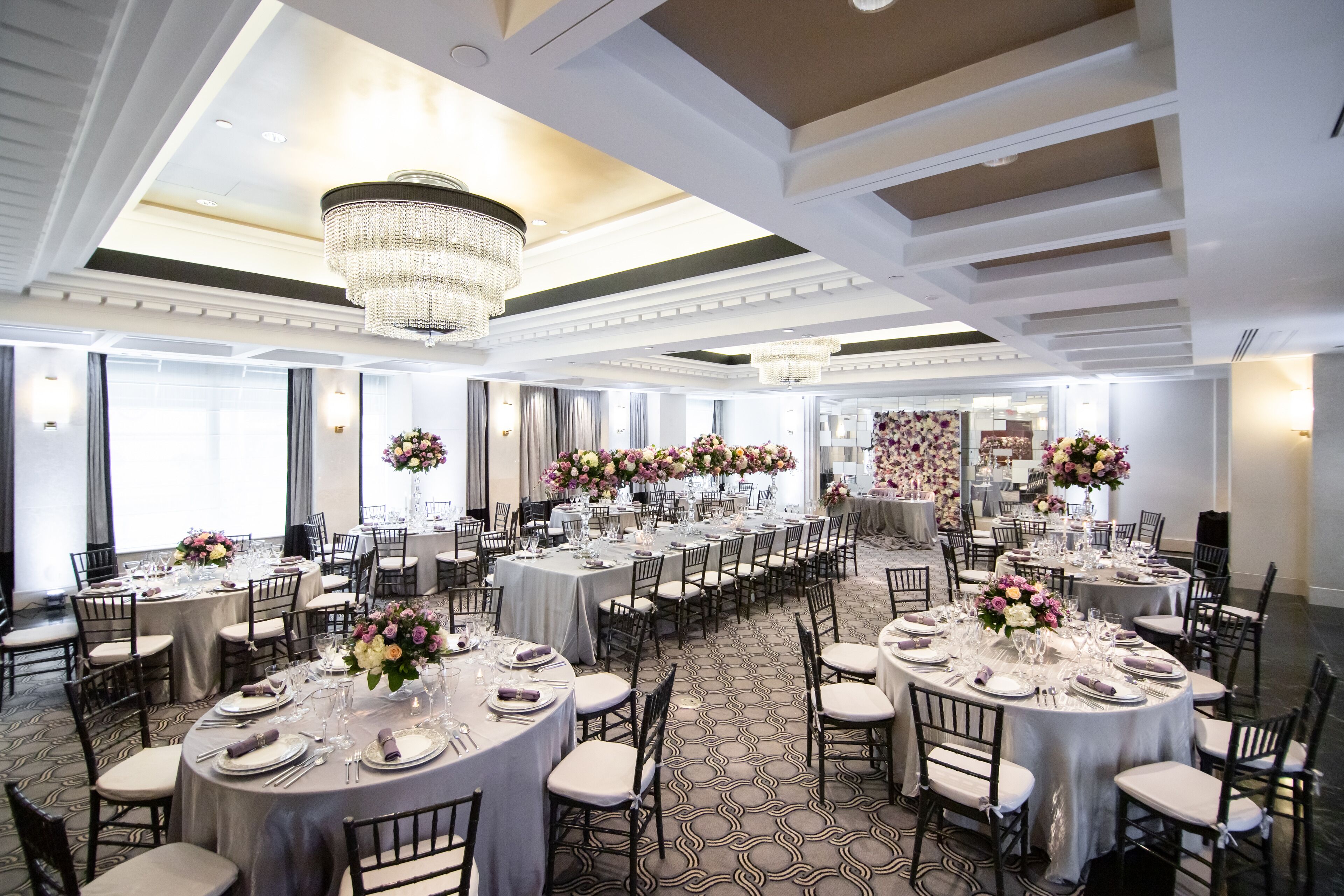 Une salle de banquet avec des tables rondes dressées pour le repas, agrémentée de lustres et de compositions florales.
