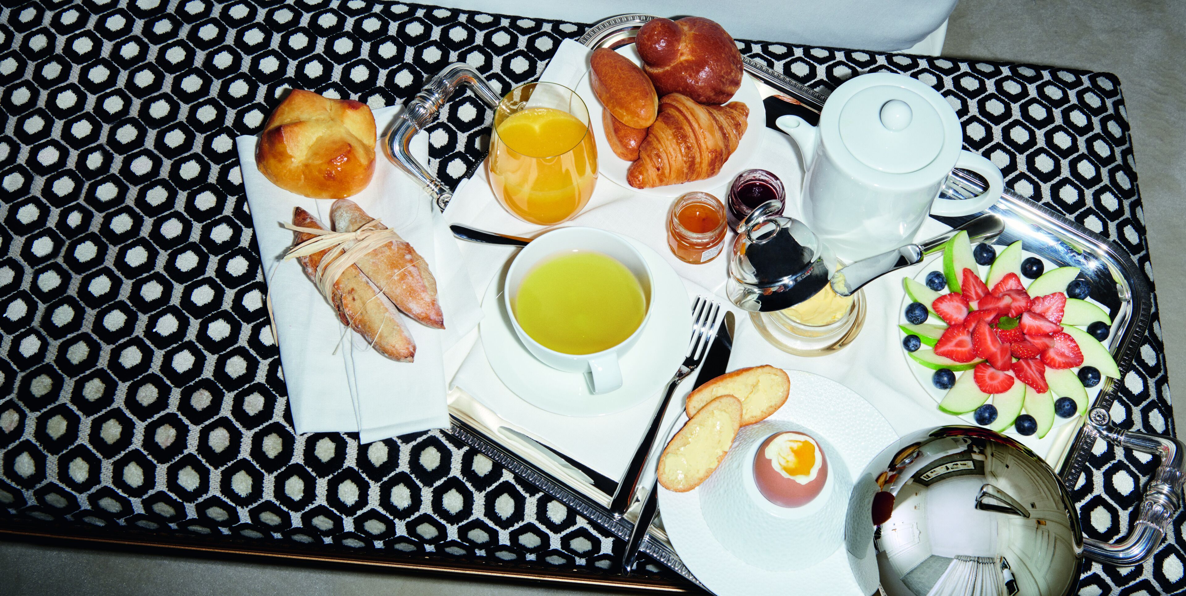 A breakfast tray with croissants, bread, fruit, and beverages.