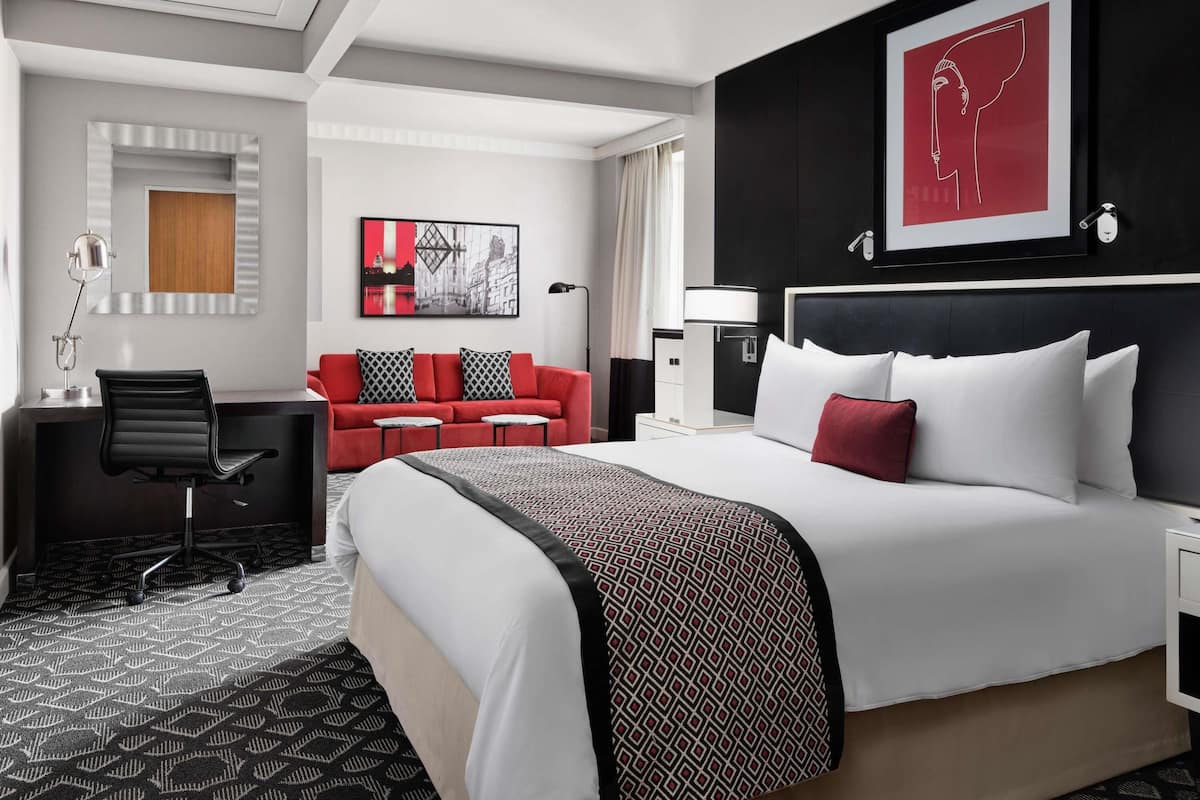 A hotel room with a bed, desk, chair, and artwork on the walls.