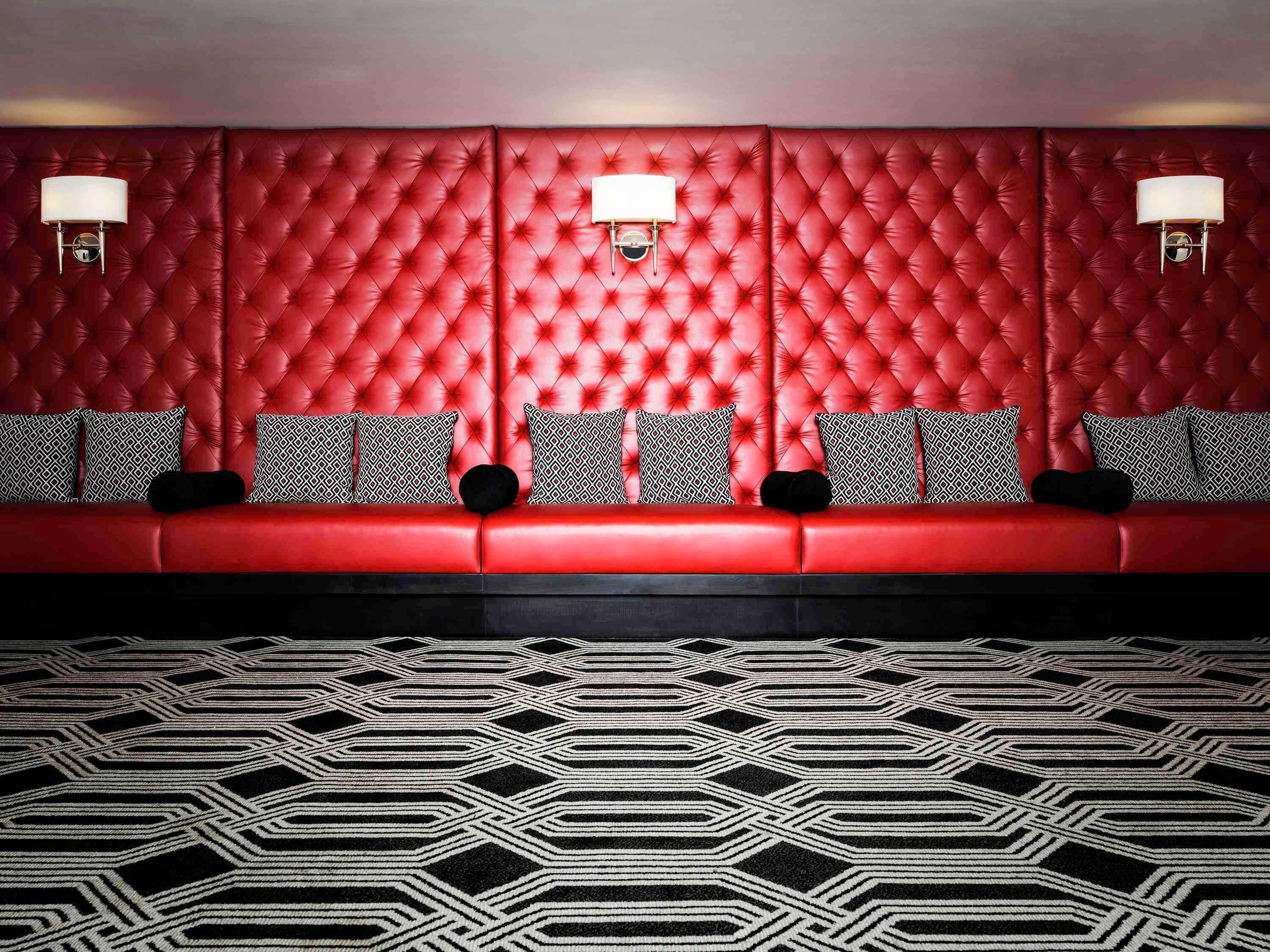 A red upholstered sofa with patterned cushions, a geometric patterned carpet, and wall-mounted lamps.