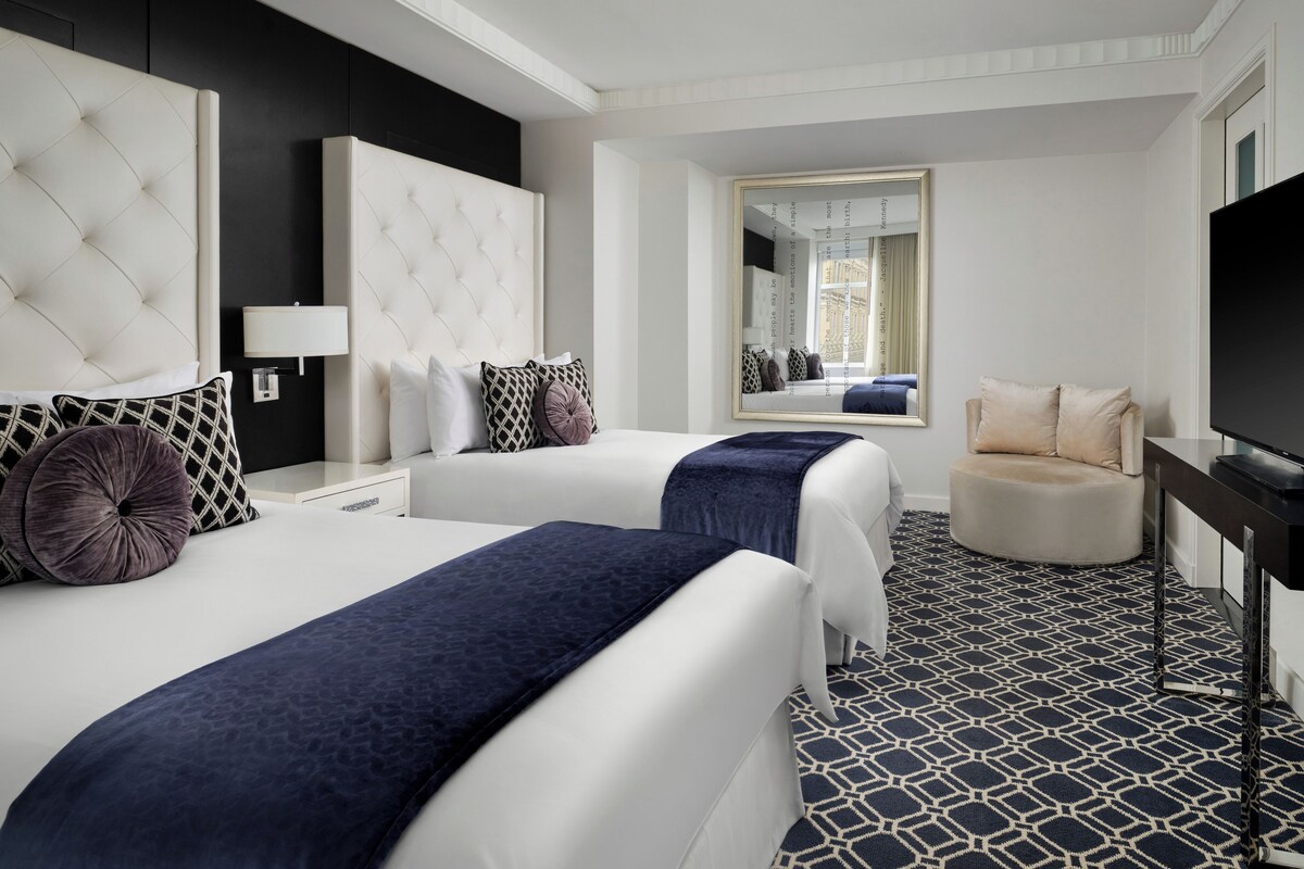 A hotel room with two beds, a TV, a sofa, and a large mirror.