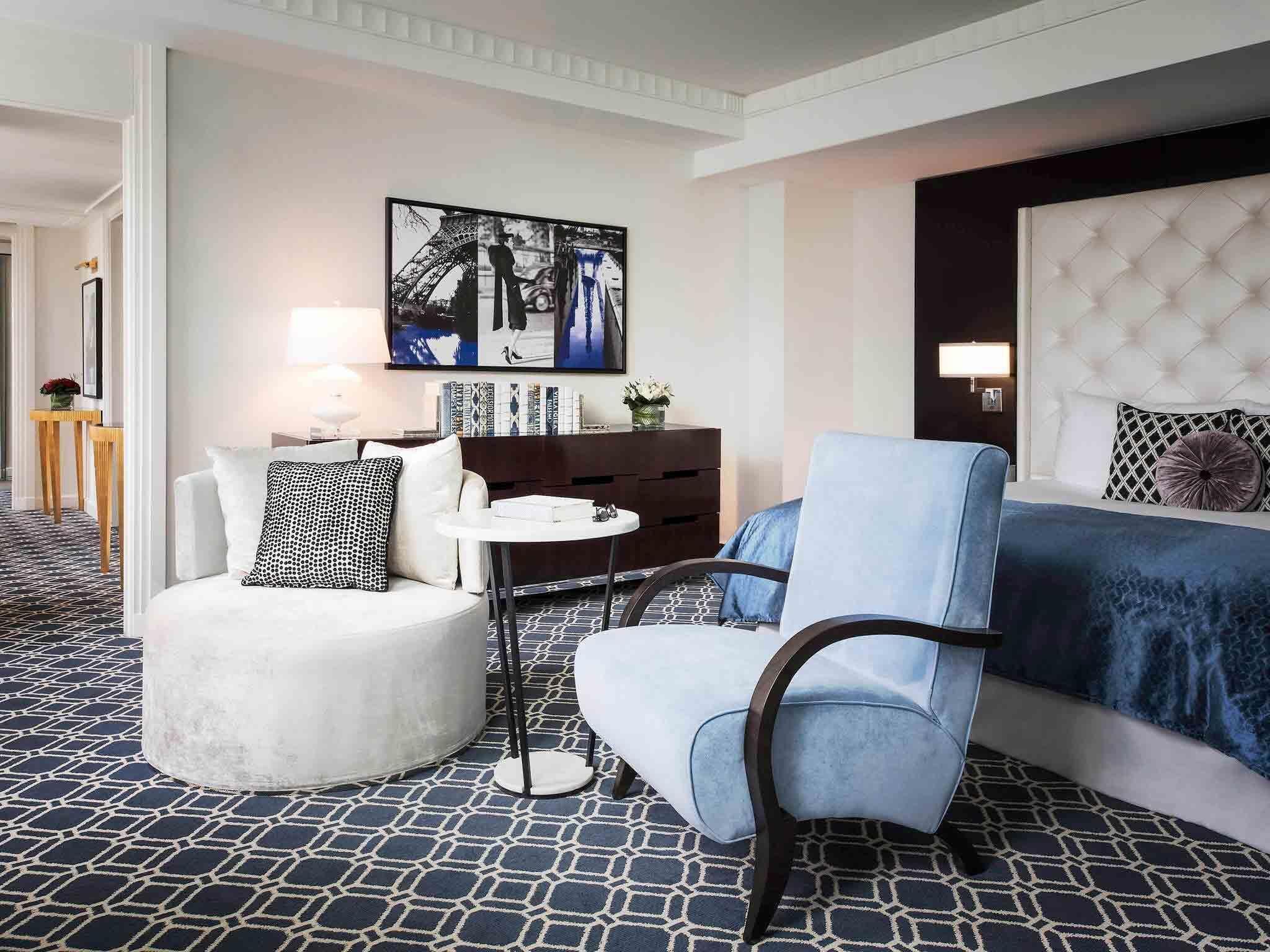 Ein Hotelzimmer mit Bett, Sessel, kleinem Tisch und Bücherregal.