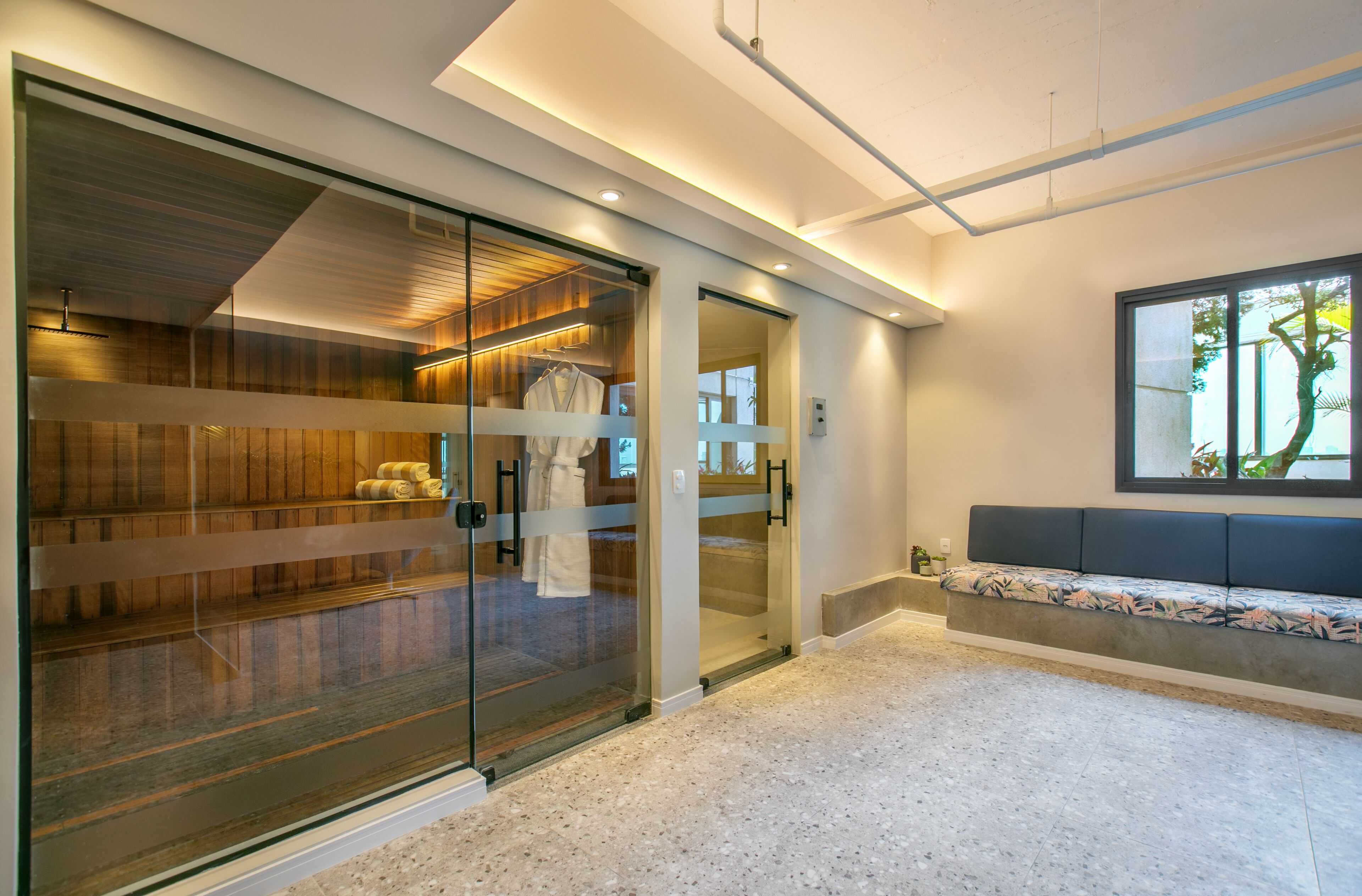 Un interior moderno con una puerta de cristal que da a una zona de almacenamiento de madera, un banco con cojín y un ventanal con vistas.
