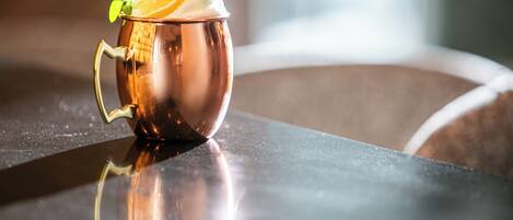 A copper mug with a mint leaf and orange slice on a reflective surface.