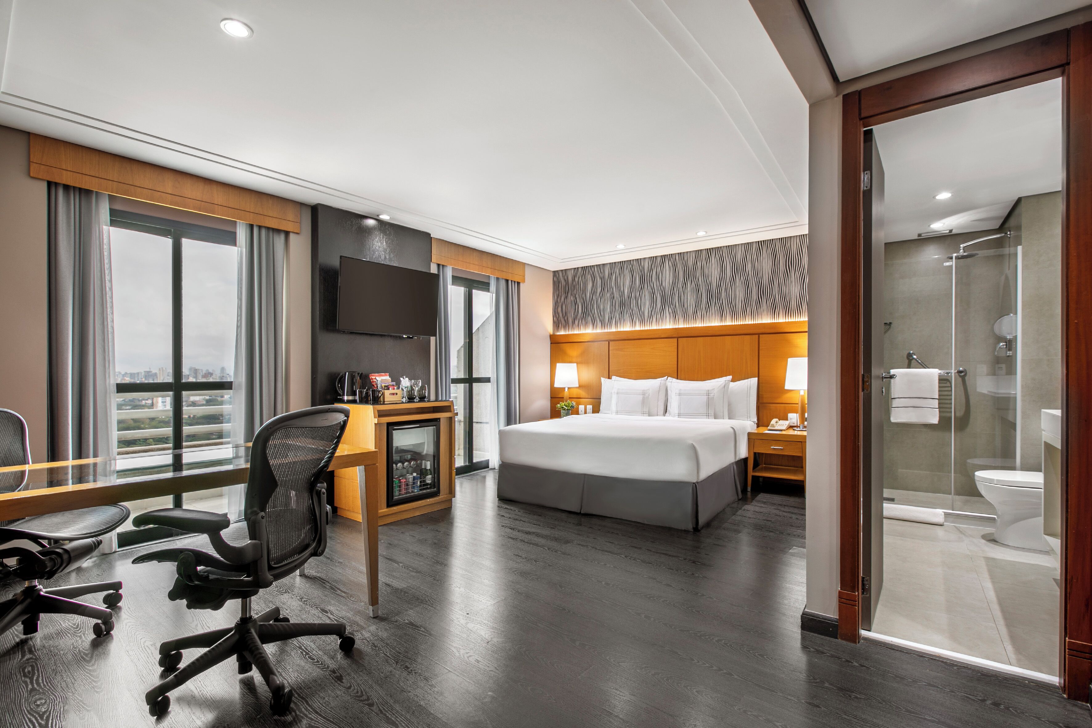 Une chambre d’hôtel avec un grand lit, un bureau avec une chaise, une télévision, un minibar et un espace douche.