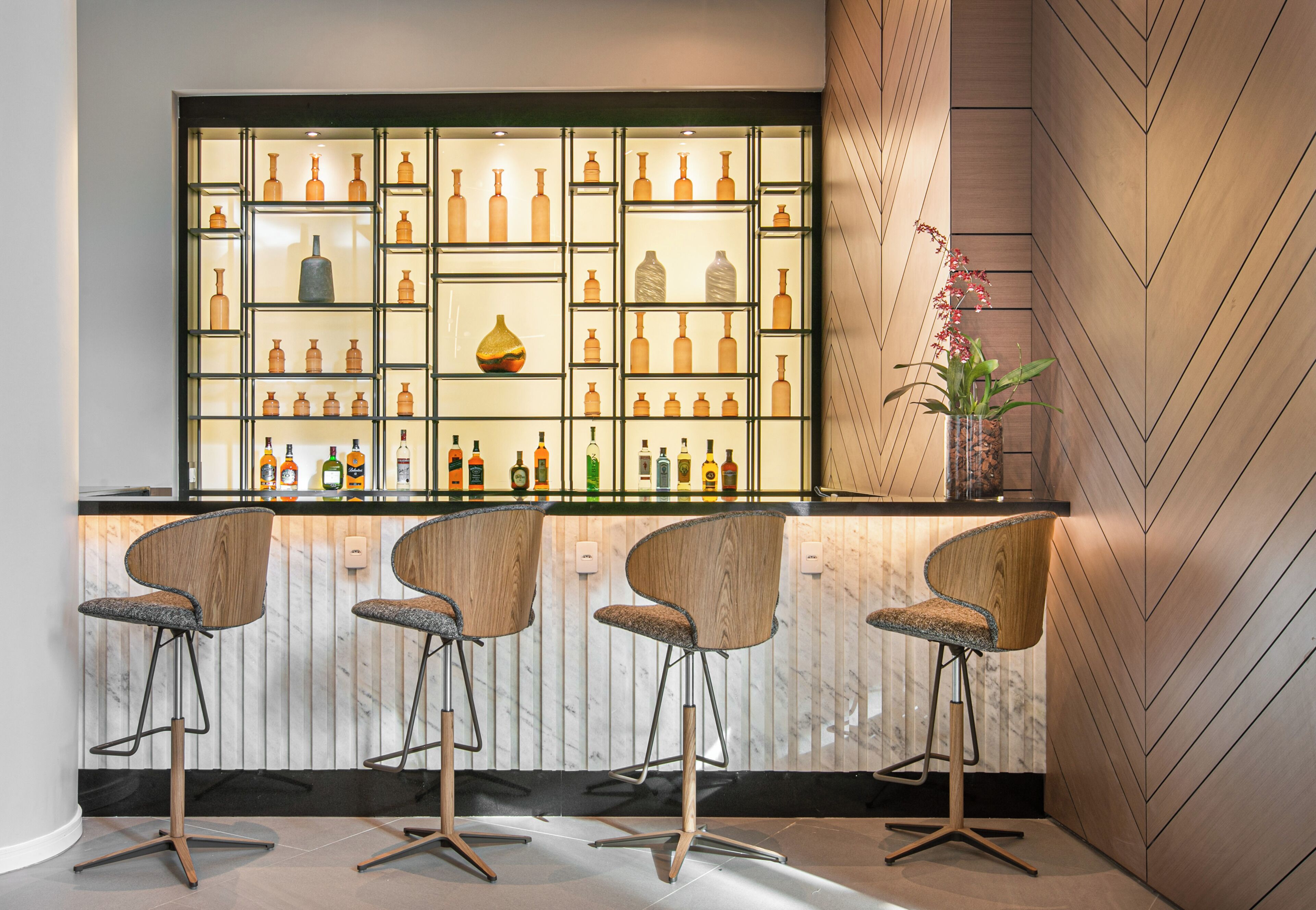A bar area with a display of bottles, three bar stools, and a potted plant.