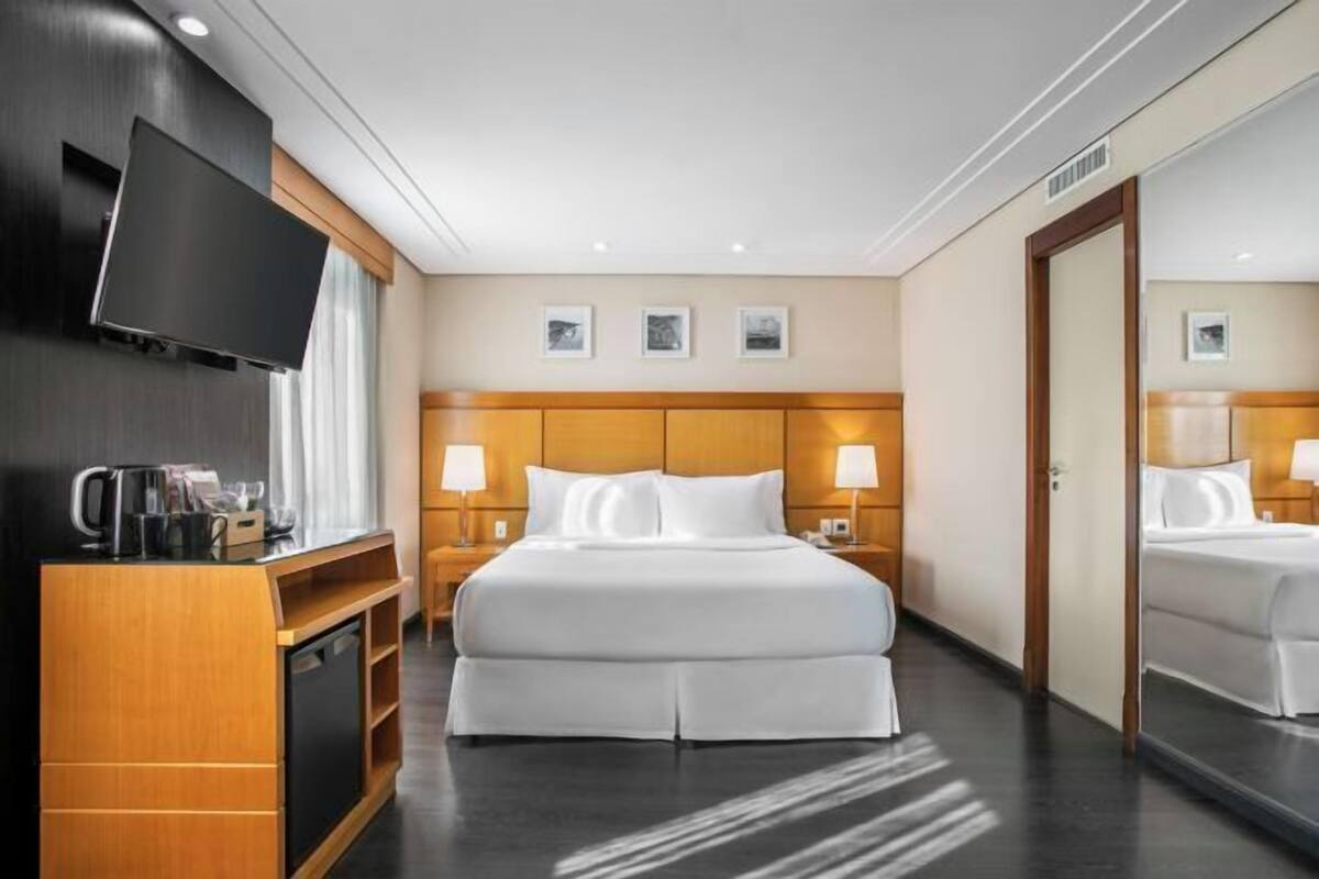 A hotel room with a bed, bedside tables, a TV, and a coffee machine.