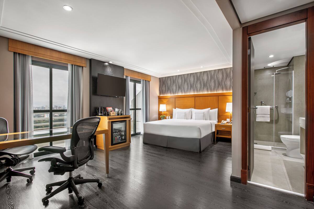 Ein Hotelzimmer mit einem großen Bett, einem Schreibtisch mit Stuhl, einem Fernseher und einem Duschbereich.